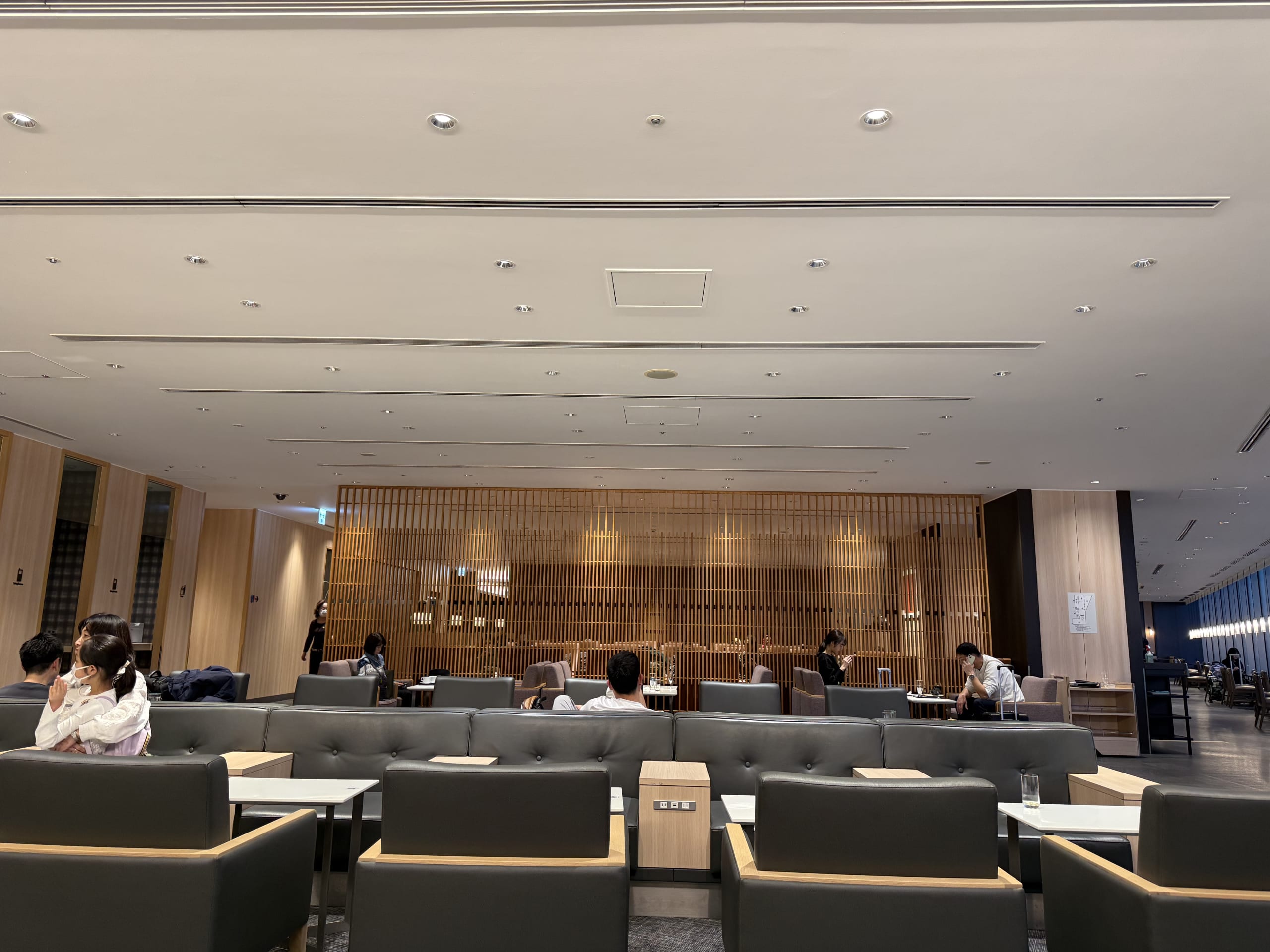 空港ラウンジで休む人々と黒いソファ、和風の木の格子。