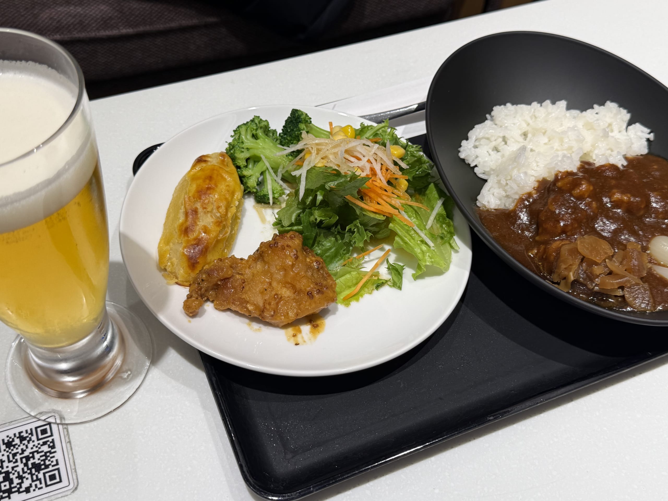 カレー、サラダ、唐揚げの皿、生ビールが置かれた机。