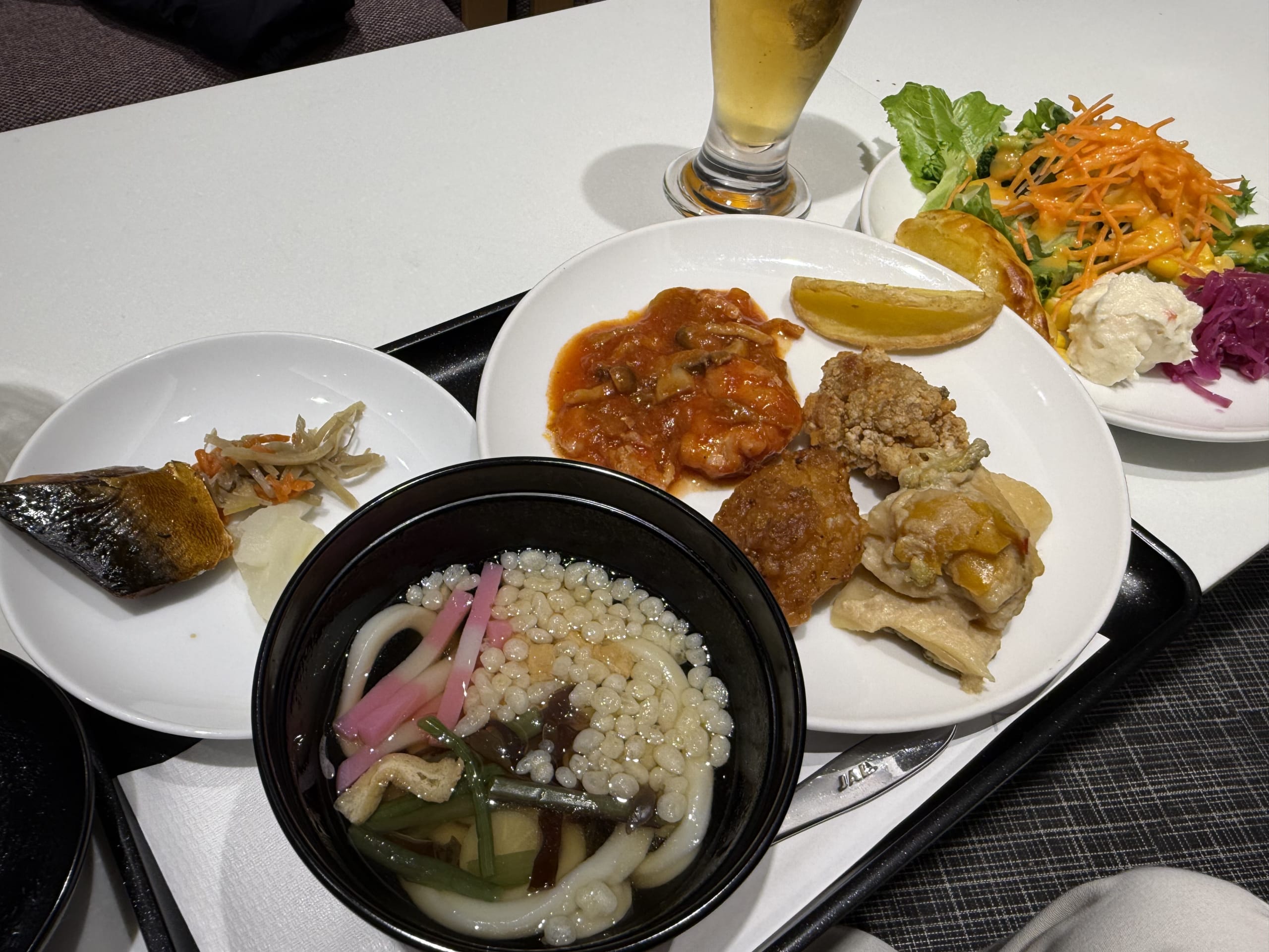 トレイに並ぶ生ビール、うどん、唐揚げ等の食事。