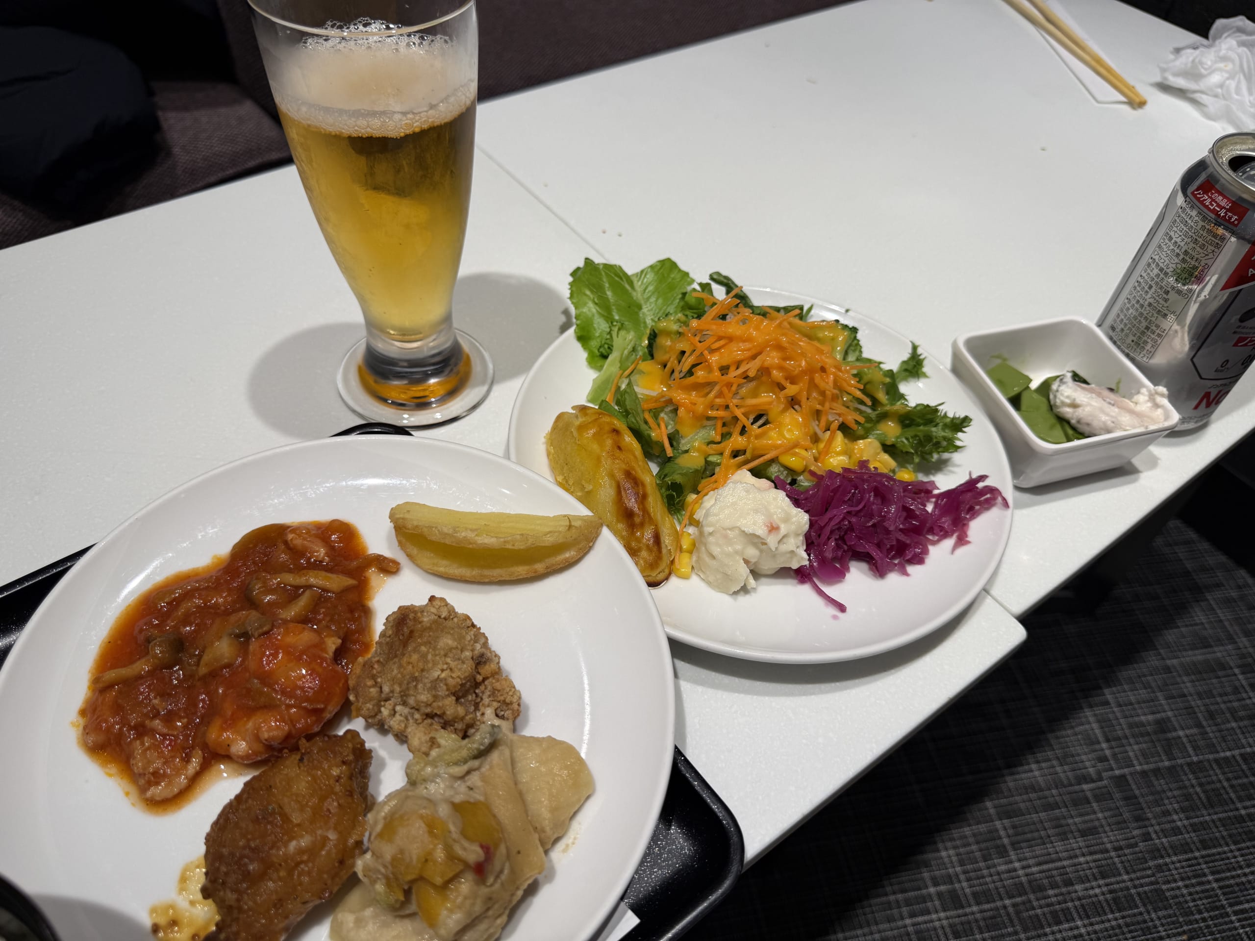 白いテーブル上のビール、サラダ、唐揚げやトマト煮が盛られた皿。