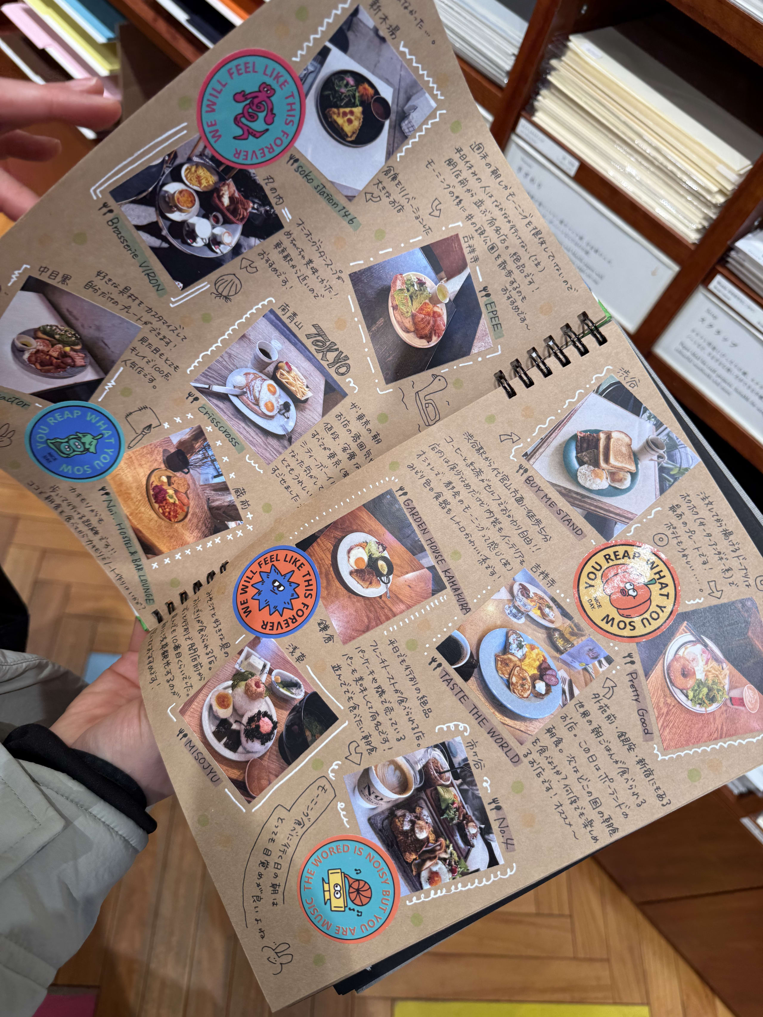 手作りの朝食スクラップブックを開く手。写真や手書きメモが貼られている。