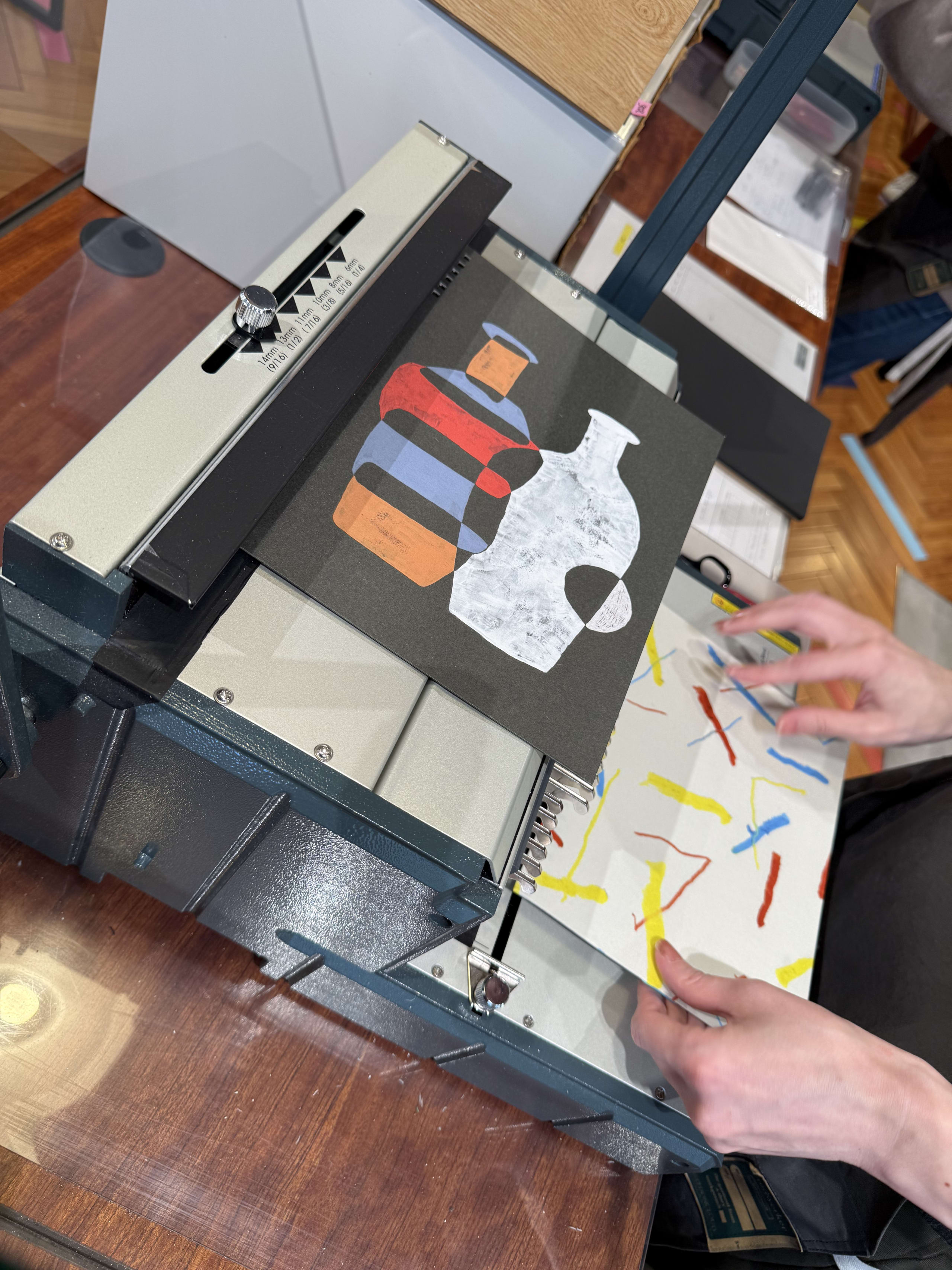 金属製の製本機にカラフルな印刷物をセットする手元。