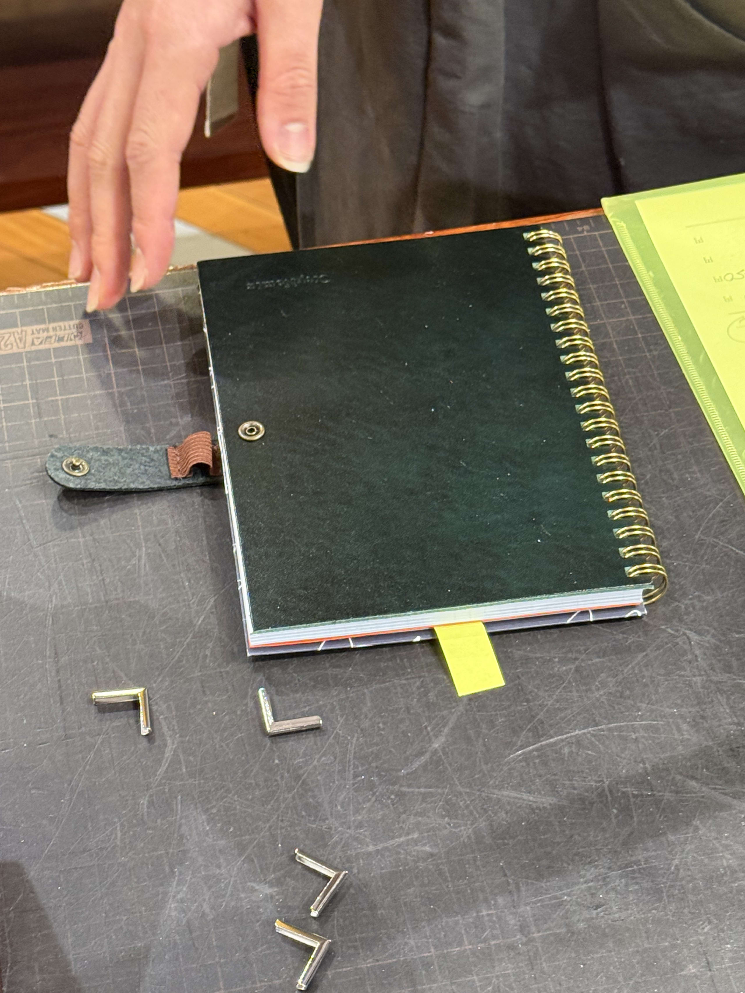 カッターマット上の黒いリングノートとコーナー金具。