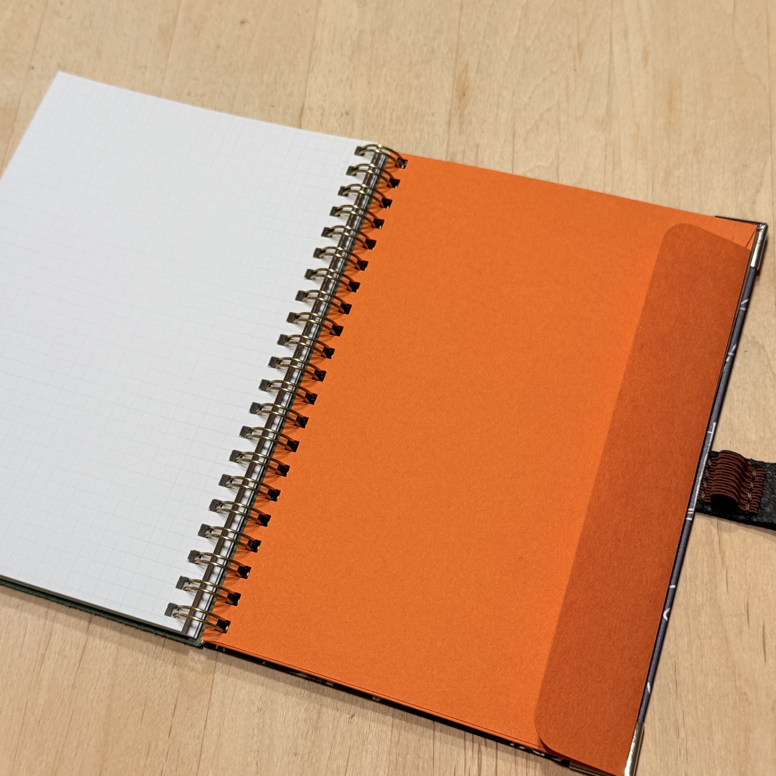 木の机に開かれたリングノート。左は方眼紙、右はオレンジのポケット。