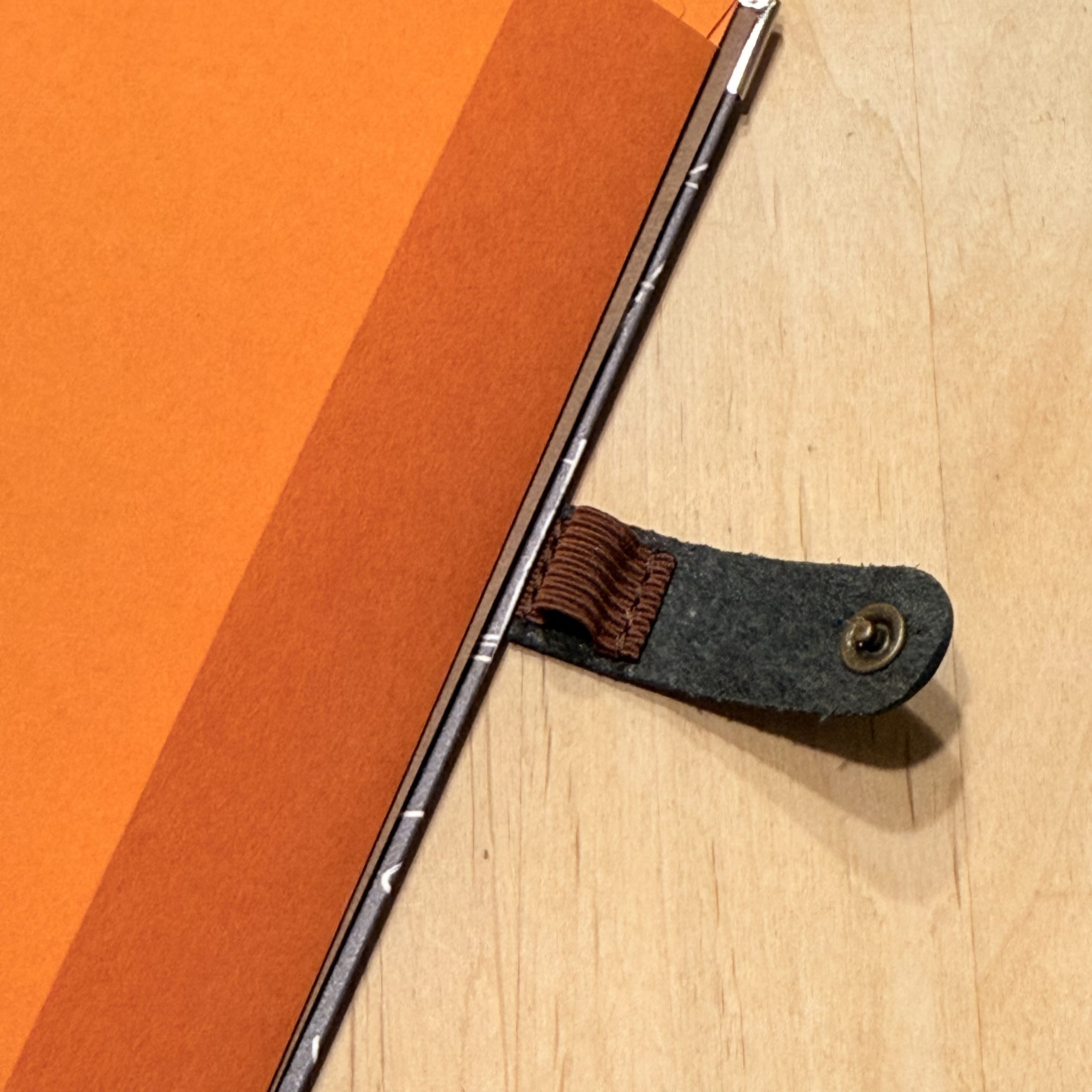 木目の机に置かれたオレンジ色のノートと革製ペンホルダー。