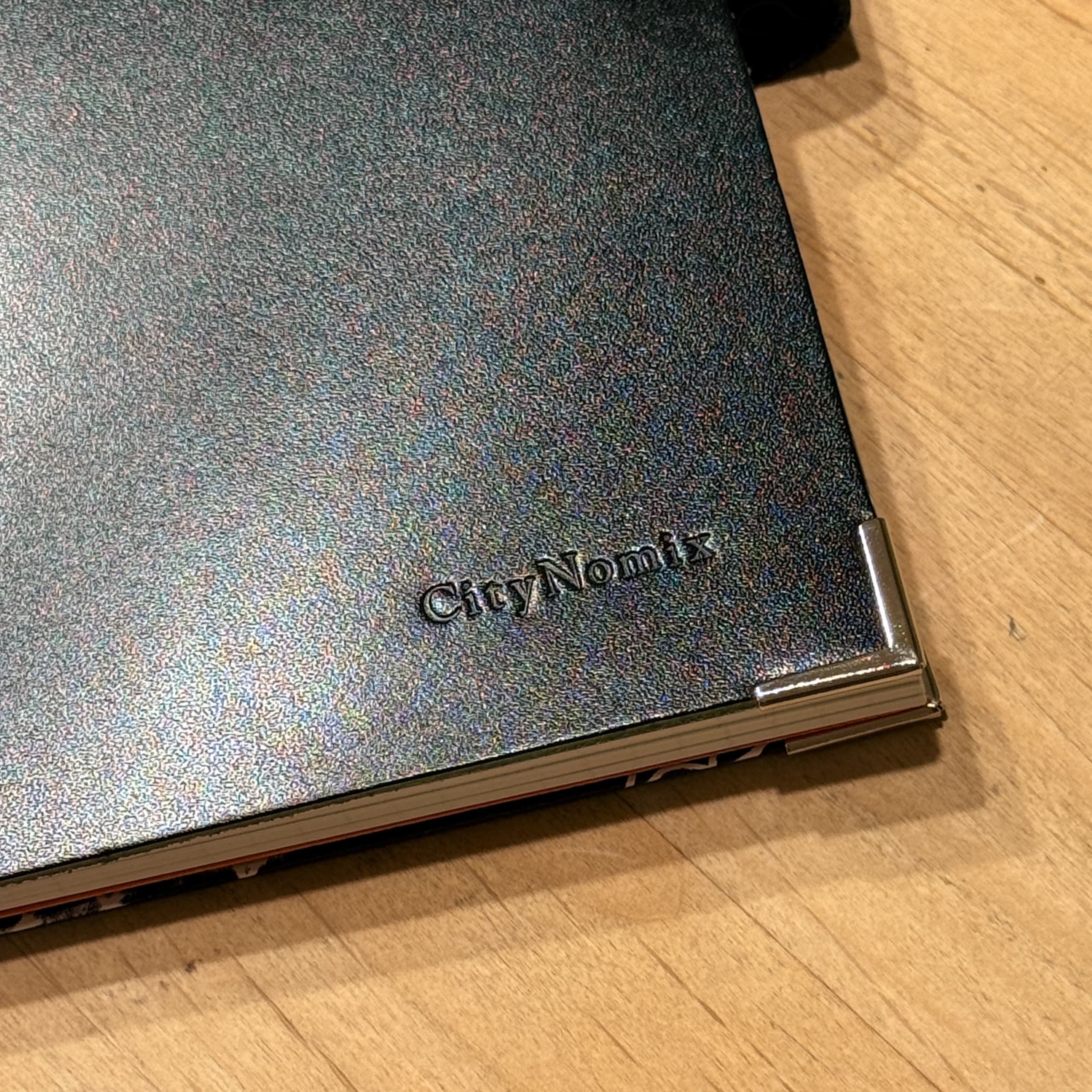 木目の机に置かれたCityNomixの刻印がある黒いノート