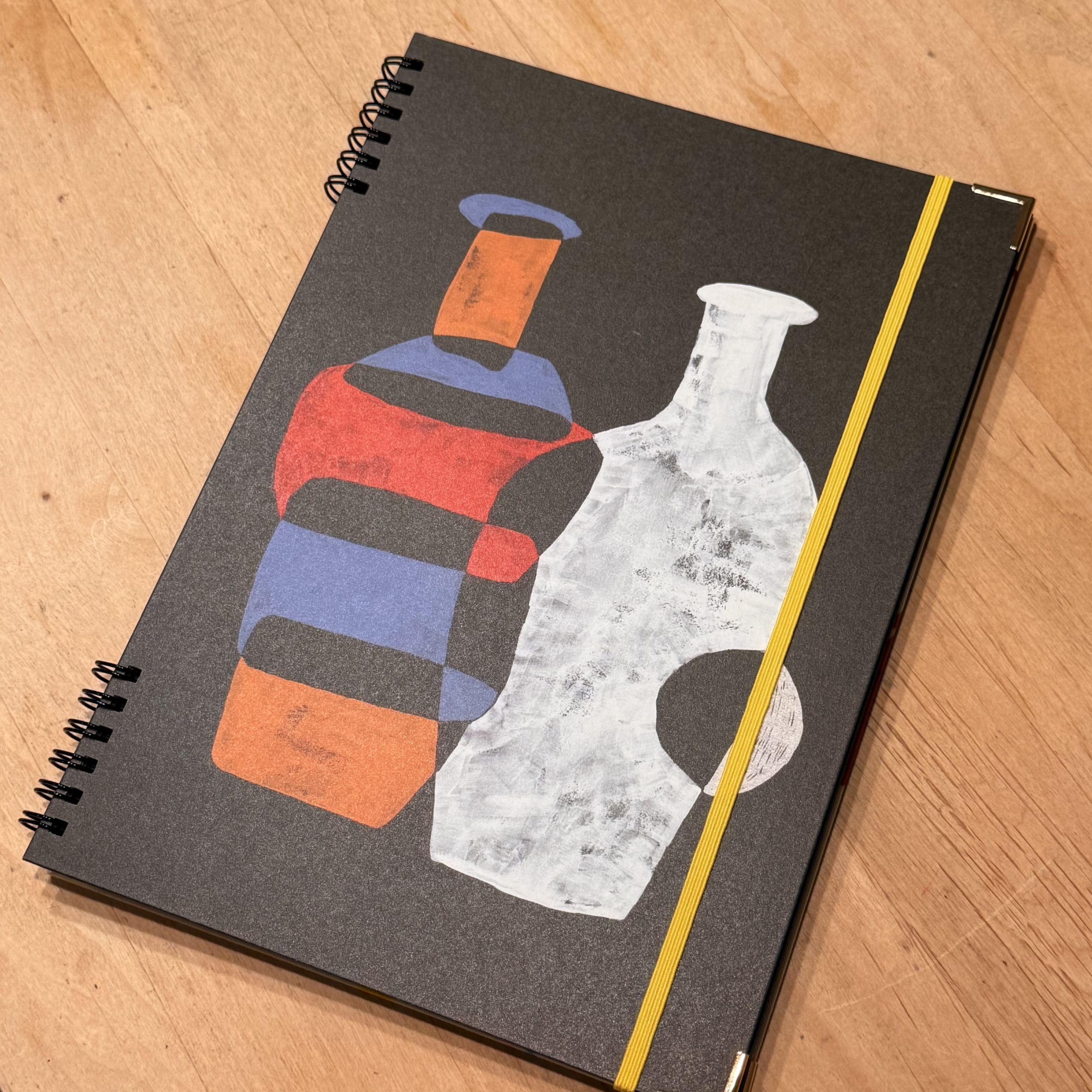 木製机の上の、ボトル柄が描かれた黒いリングノート。