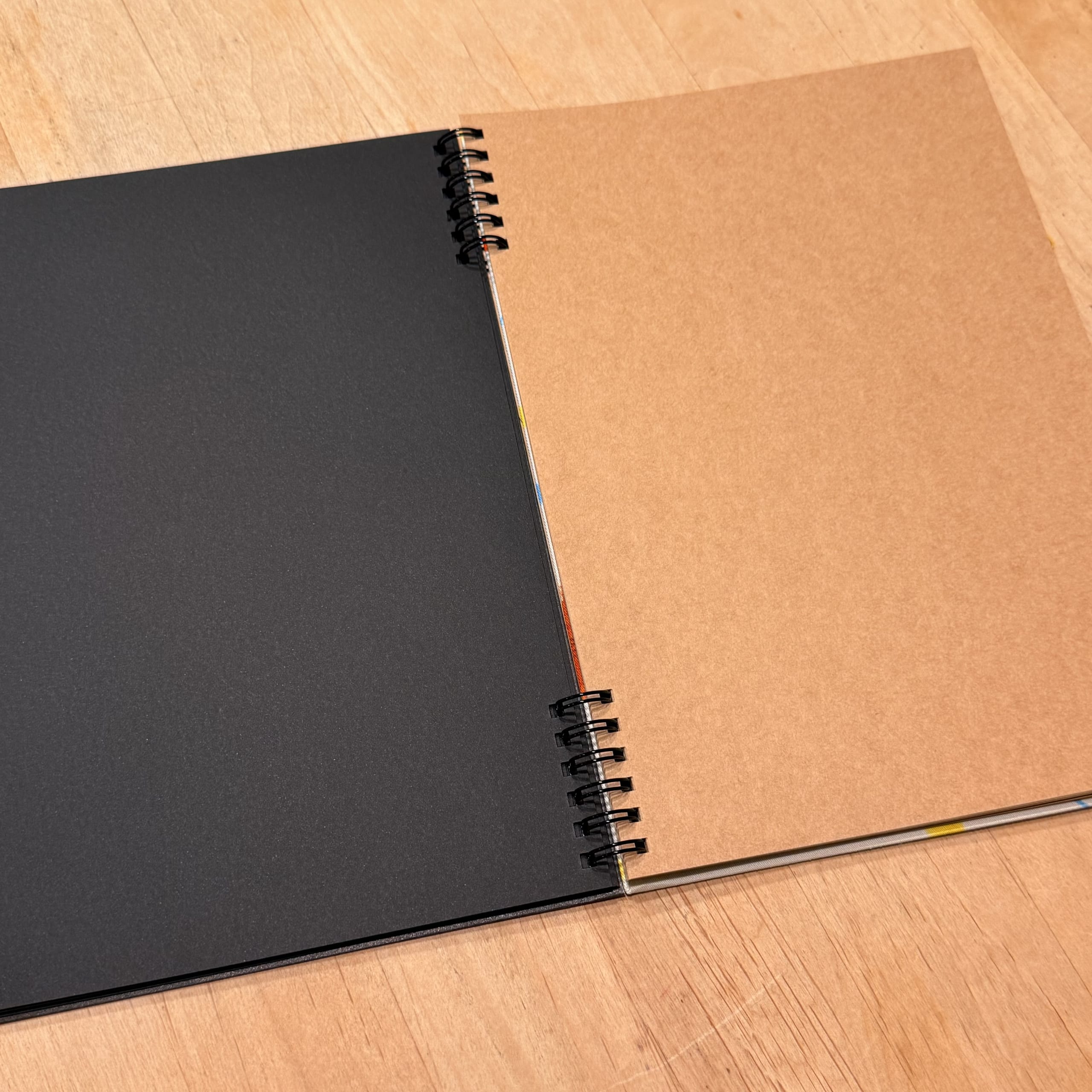 木目の机に開かれた左が黒色で右がクラフト紙のリングノート