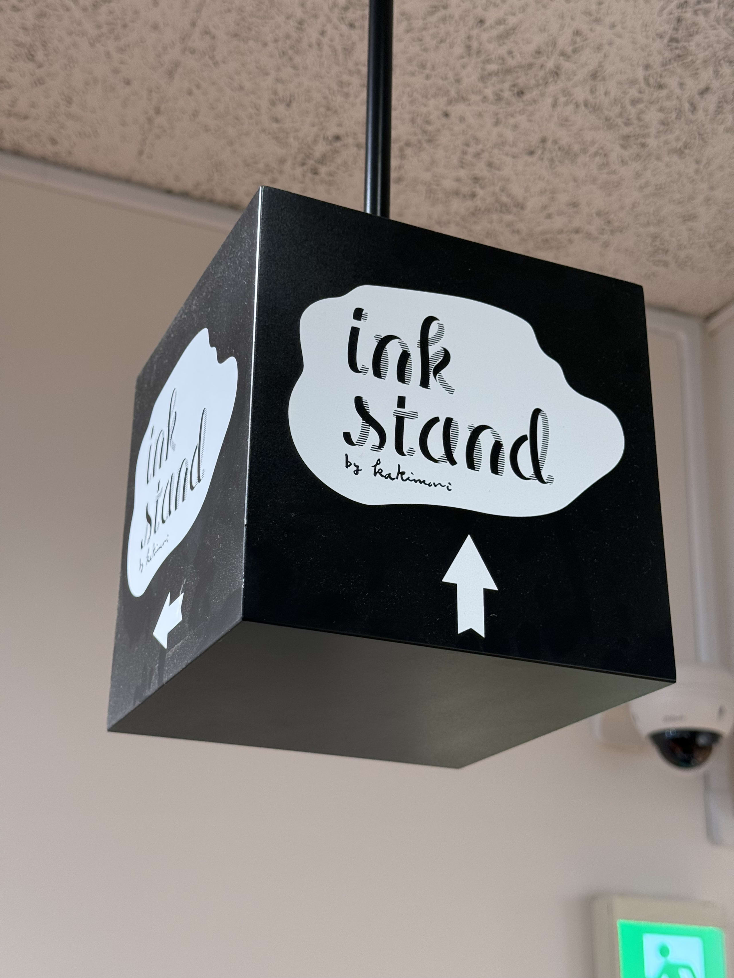 天井に吊るされたインクスタンドの黒いキューブ型看板