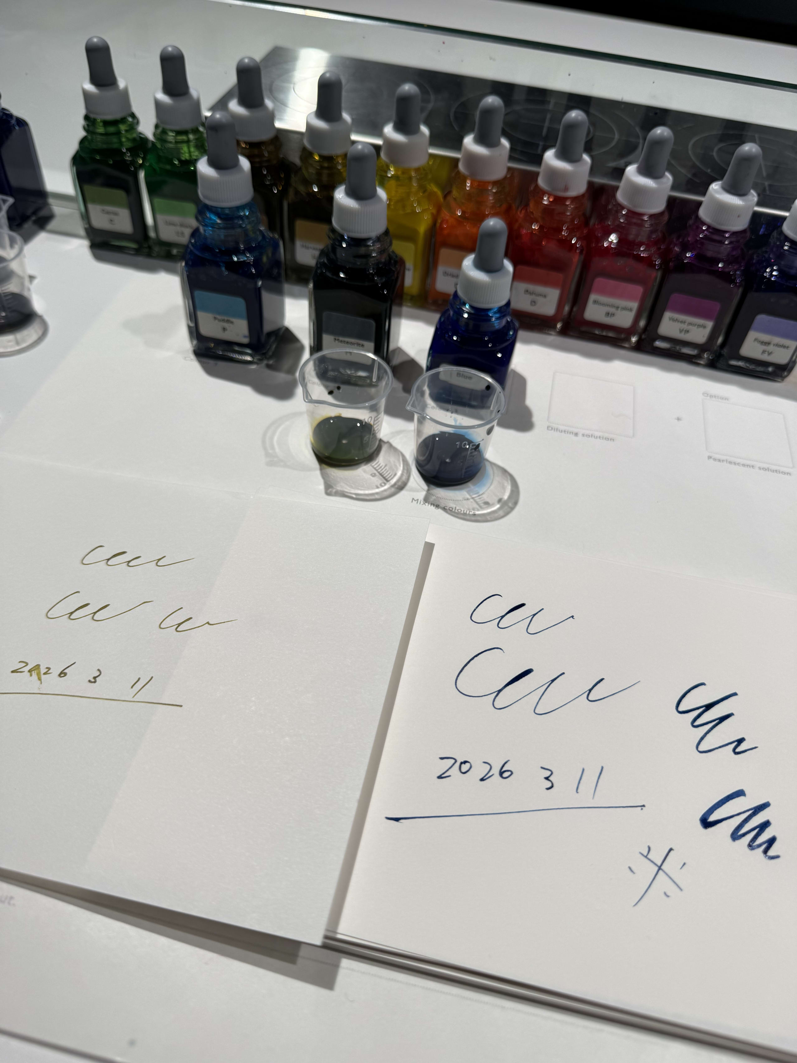 調合中インクと試し書き紙。奥に瓶が並ぶ。