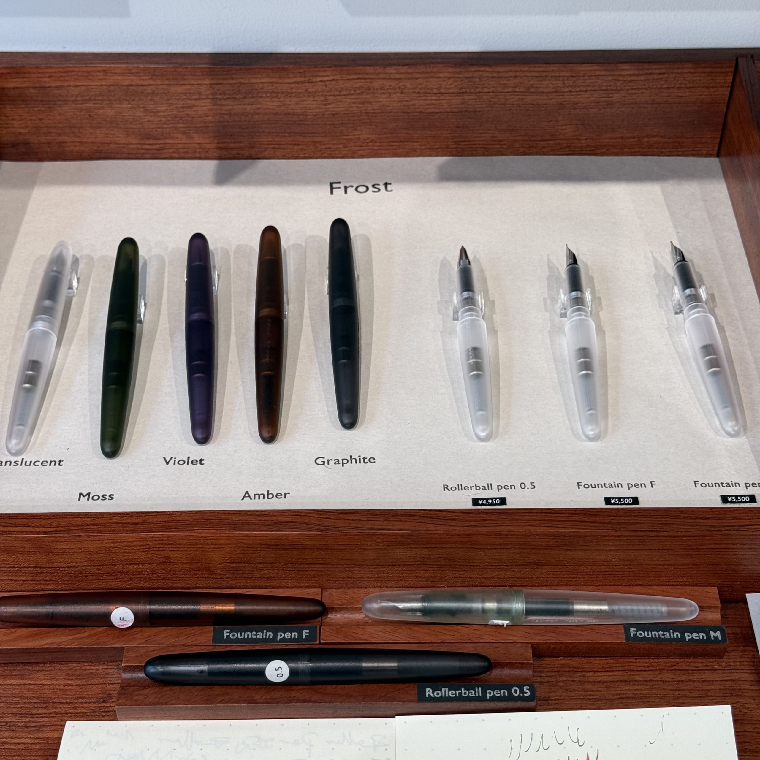 木製のケースに並ぶ半透明ボディの万年筆とローラーボール。