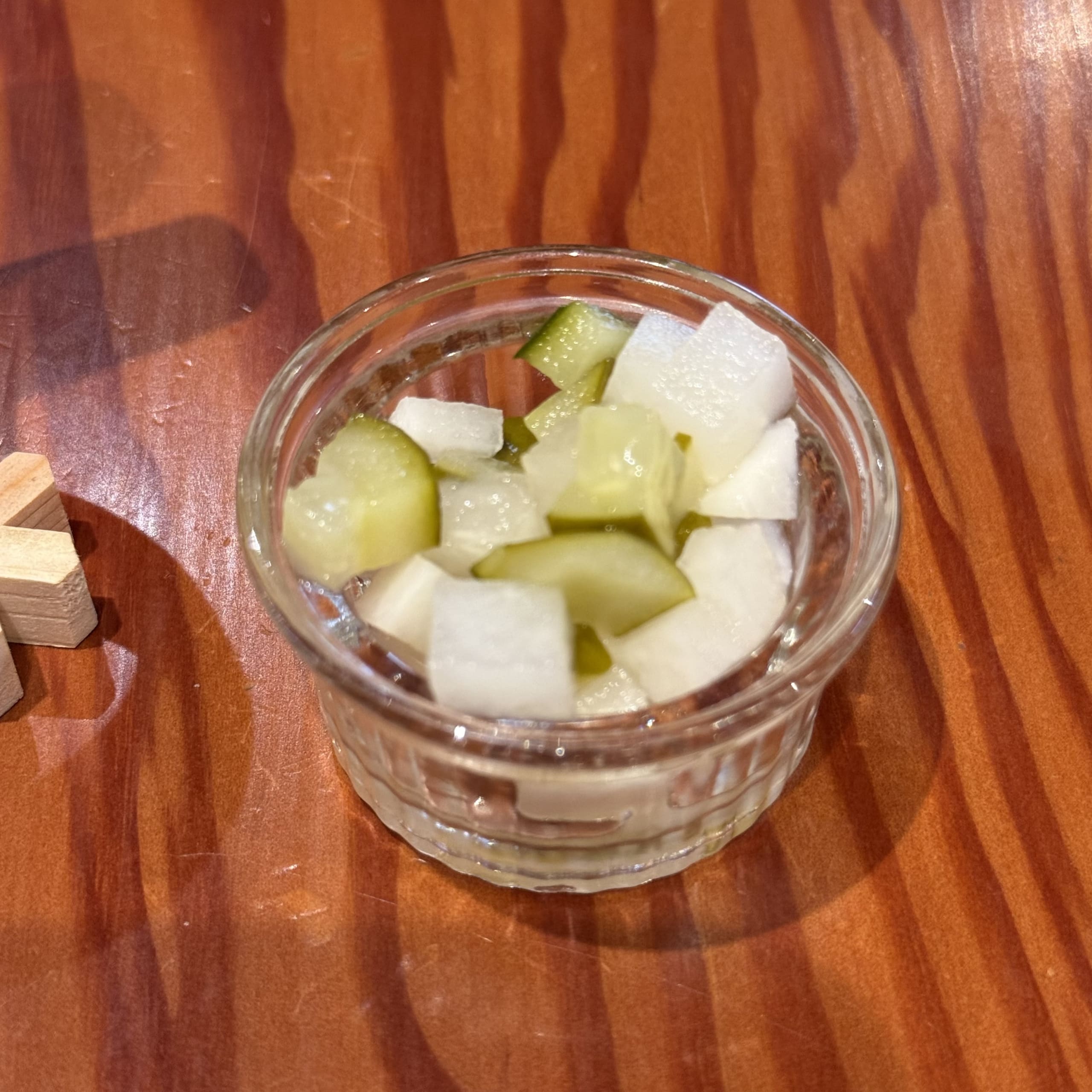 木目テーブルの上のガラス器に入った大根とキュウリのピクルス。