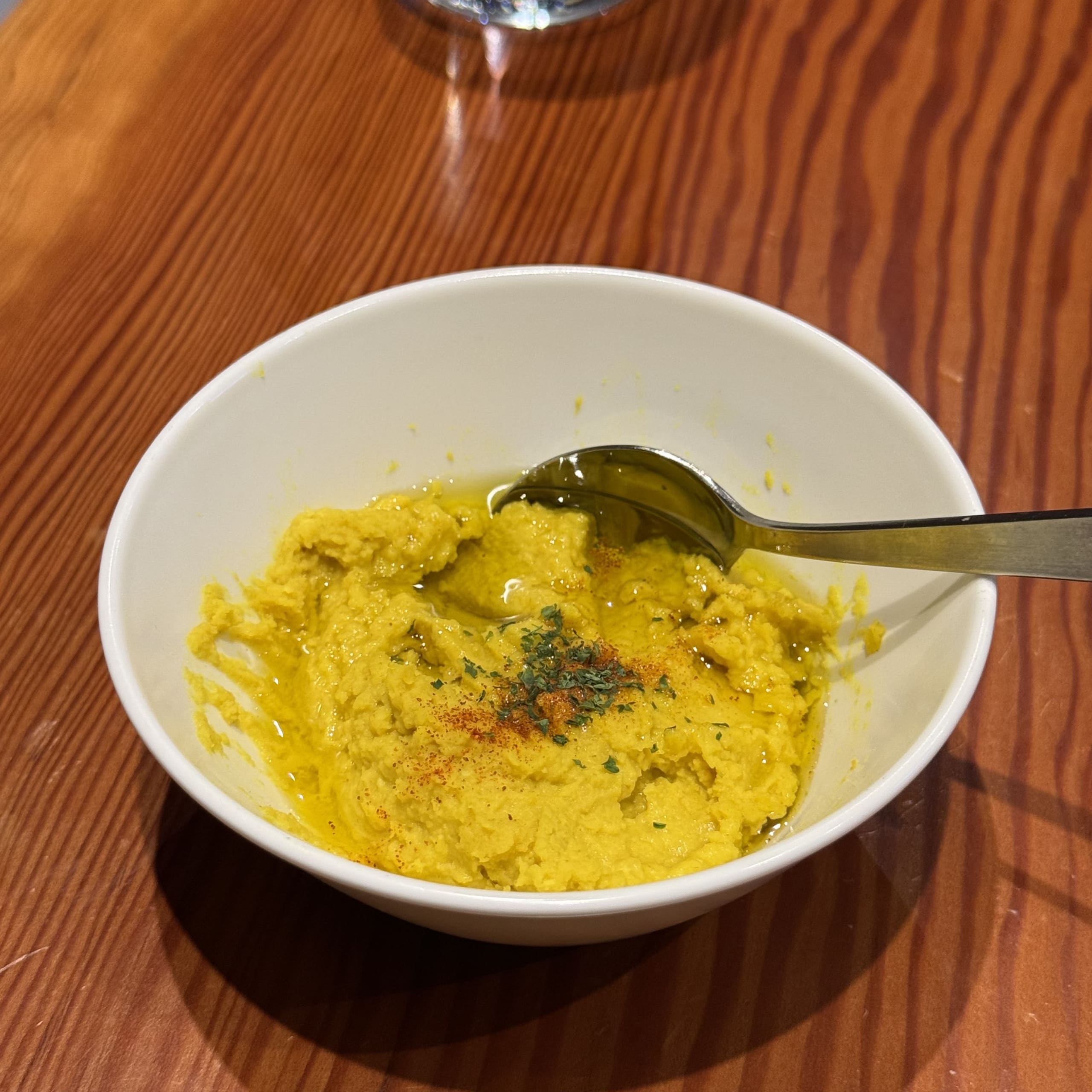 木目テーブル上の白いボウルに入った黄色のフムス。