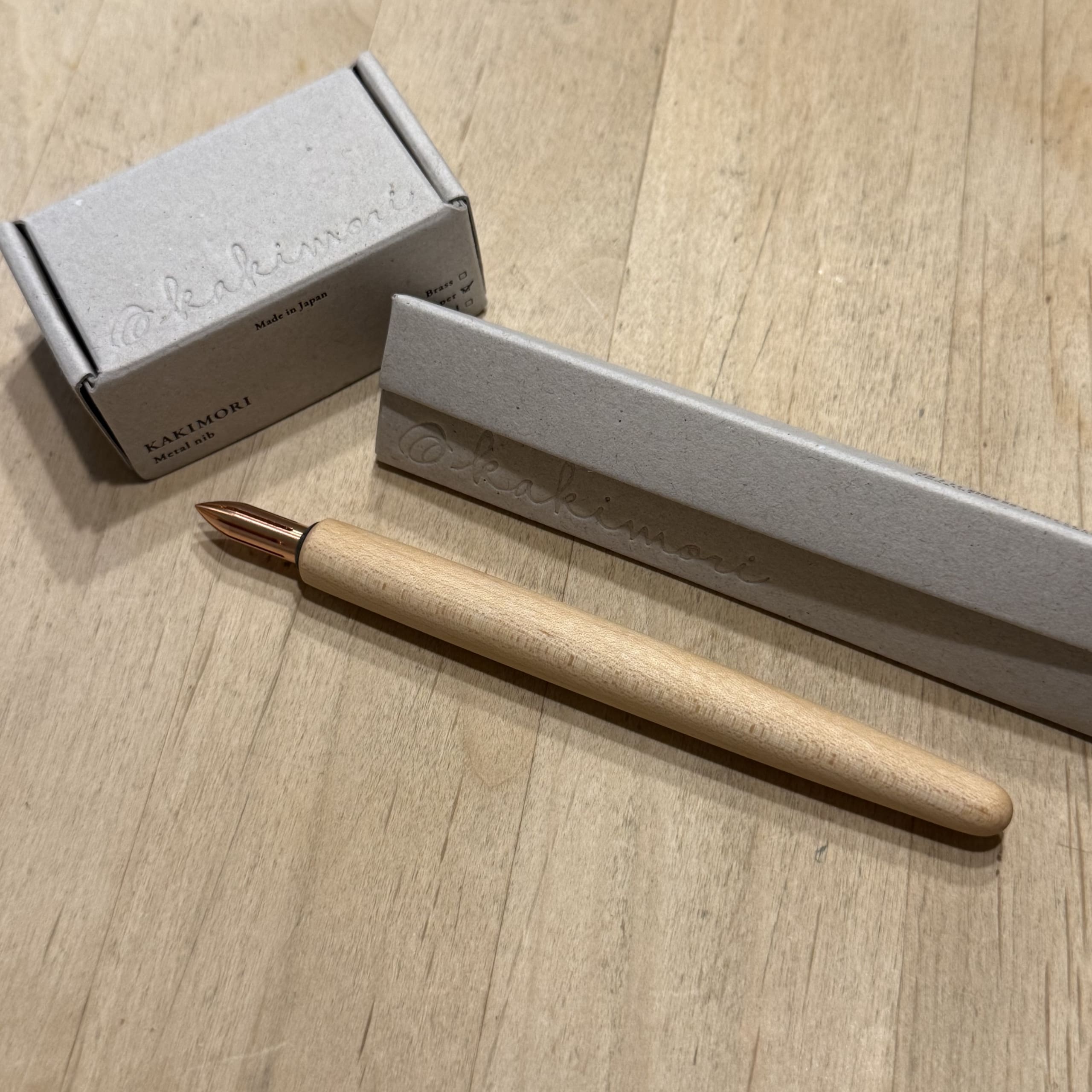 木の机にあるカキモリのつけペン、銅のペン先、グレーの小箱。