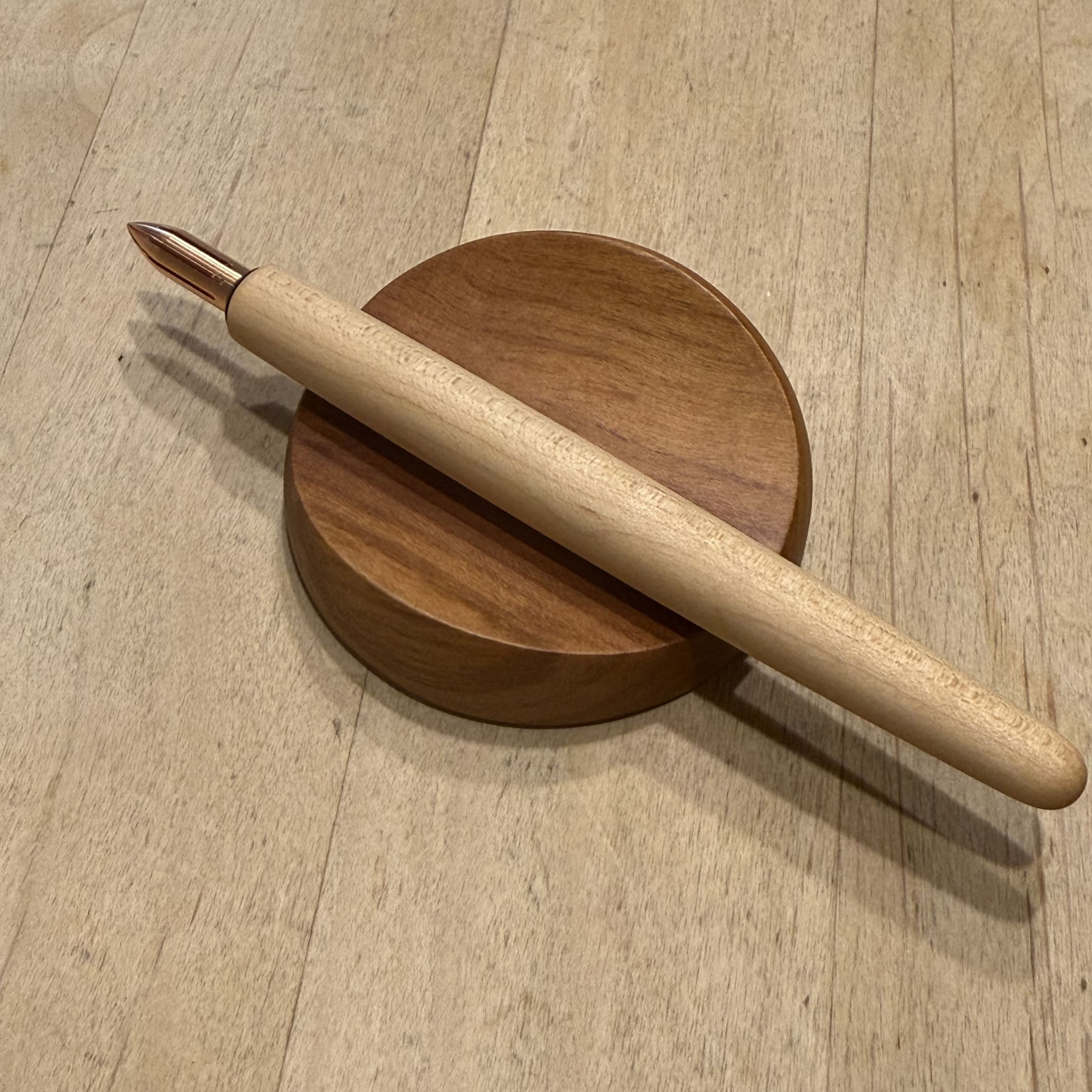 丸い木製トレイに置かれた銅製ペン先の木軸つけペン。