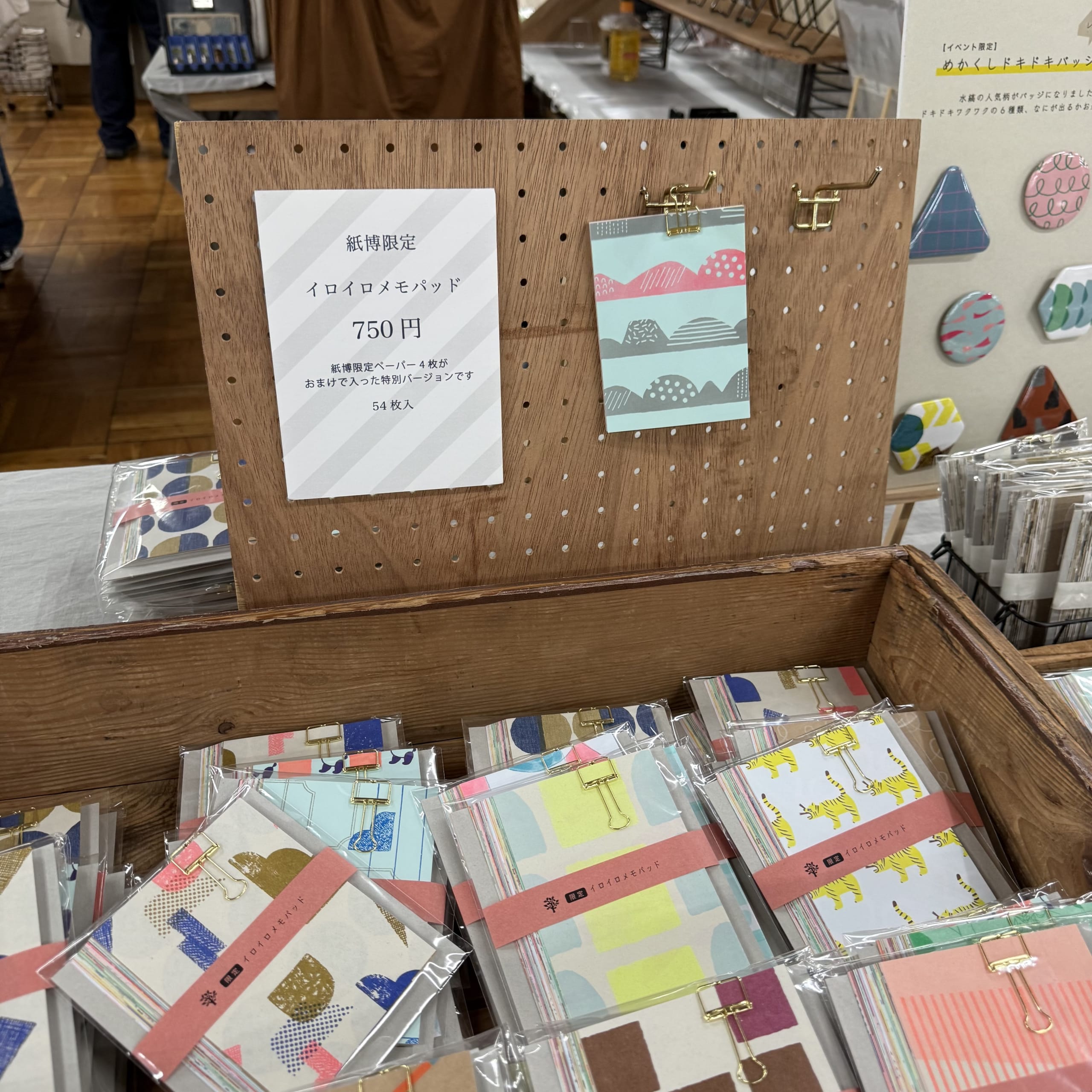 木箱に並ぶ多彩な柄のメモパッドと紙博限定のポップ。