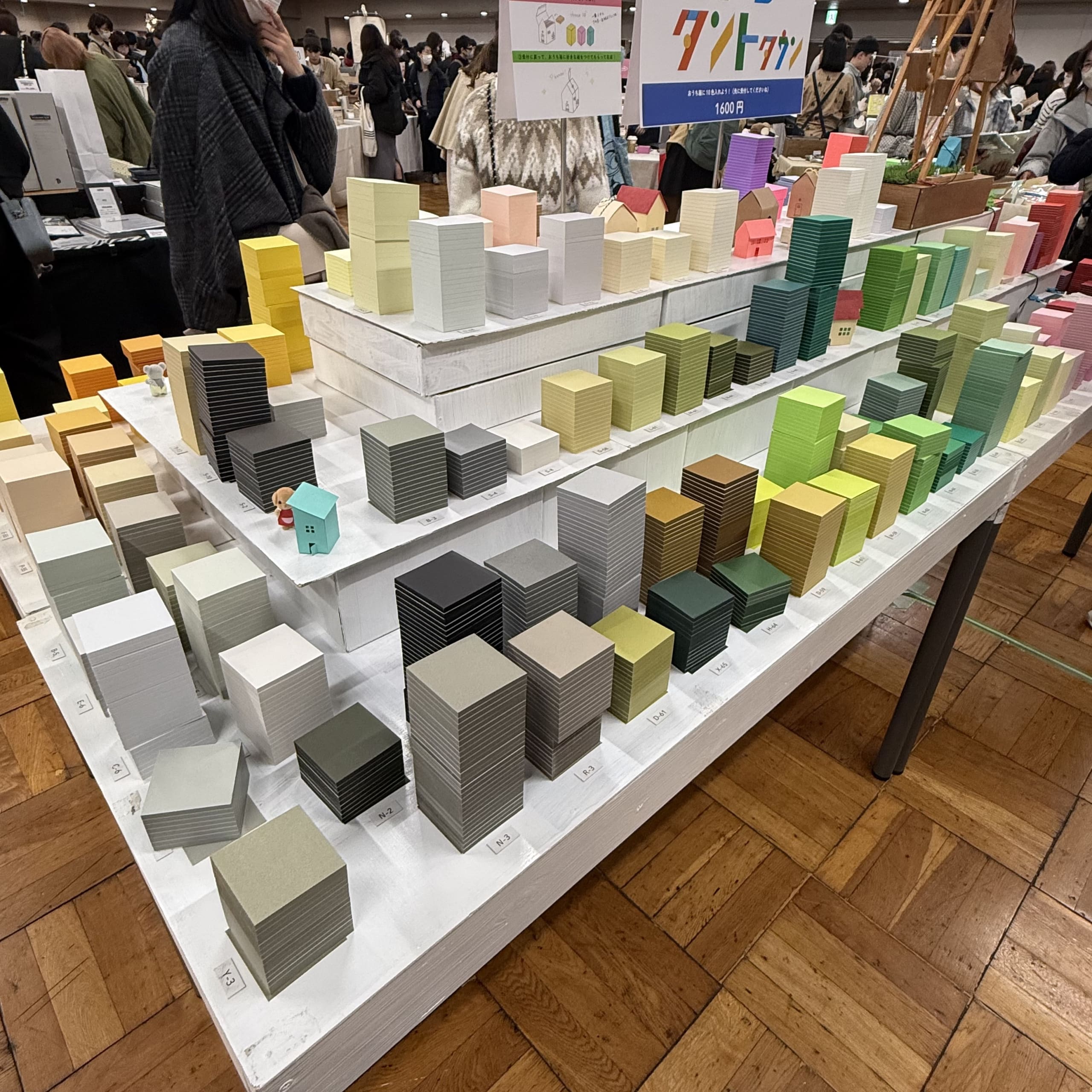 ビル群のように積まれた色鮮やかな紙の束と多くの来場者。