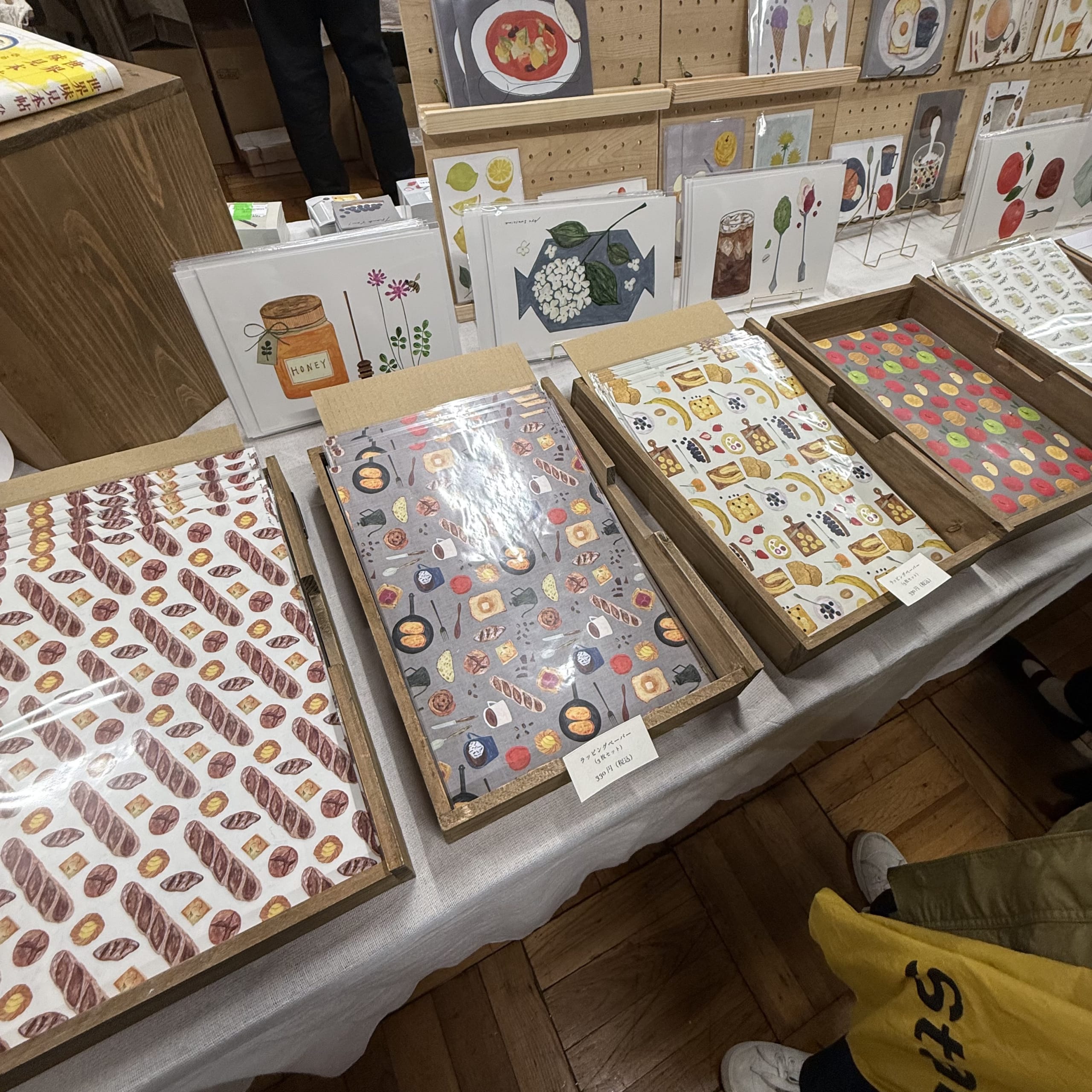 パンや果物柄の包装紙が木箱に並ぶ紙モノ販売ブース。