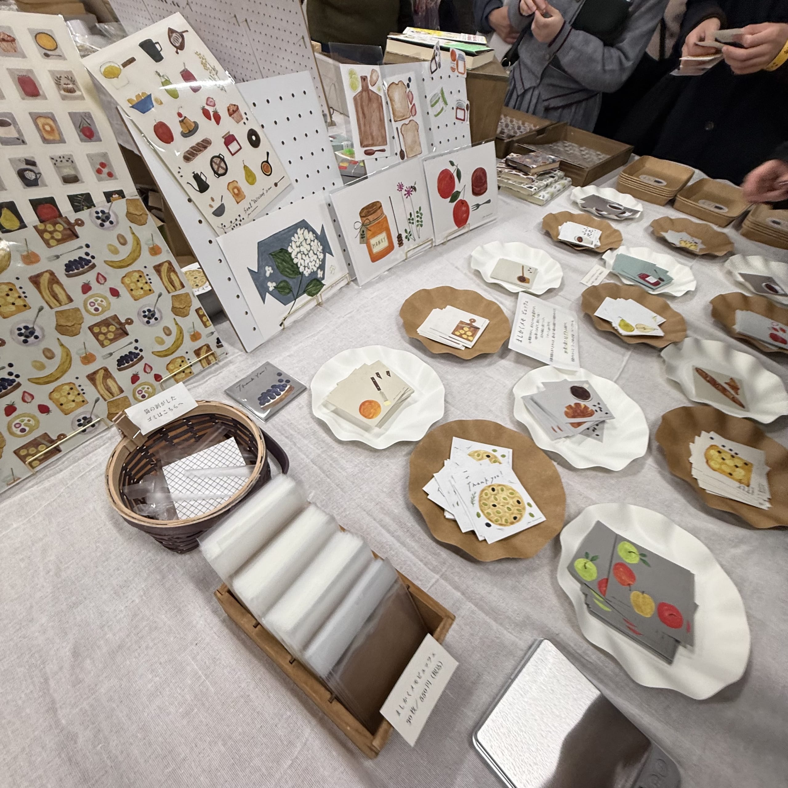 白い机上のイラスト入りメモと選んで取る客の手。