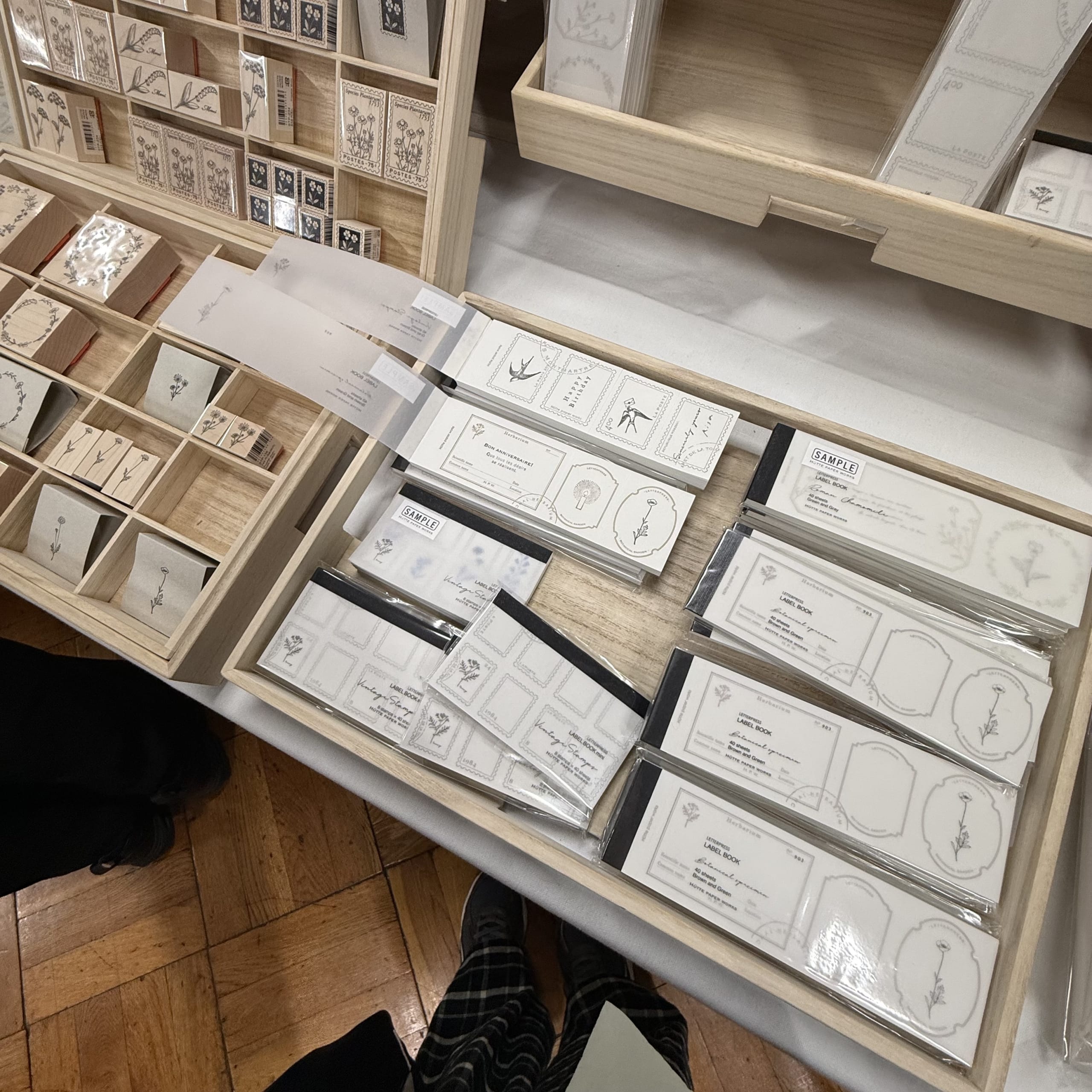 木製トレイに並ぶ植物柄のスタンプやラベルブックと客の足元。