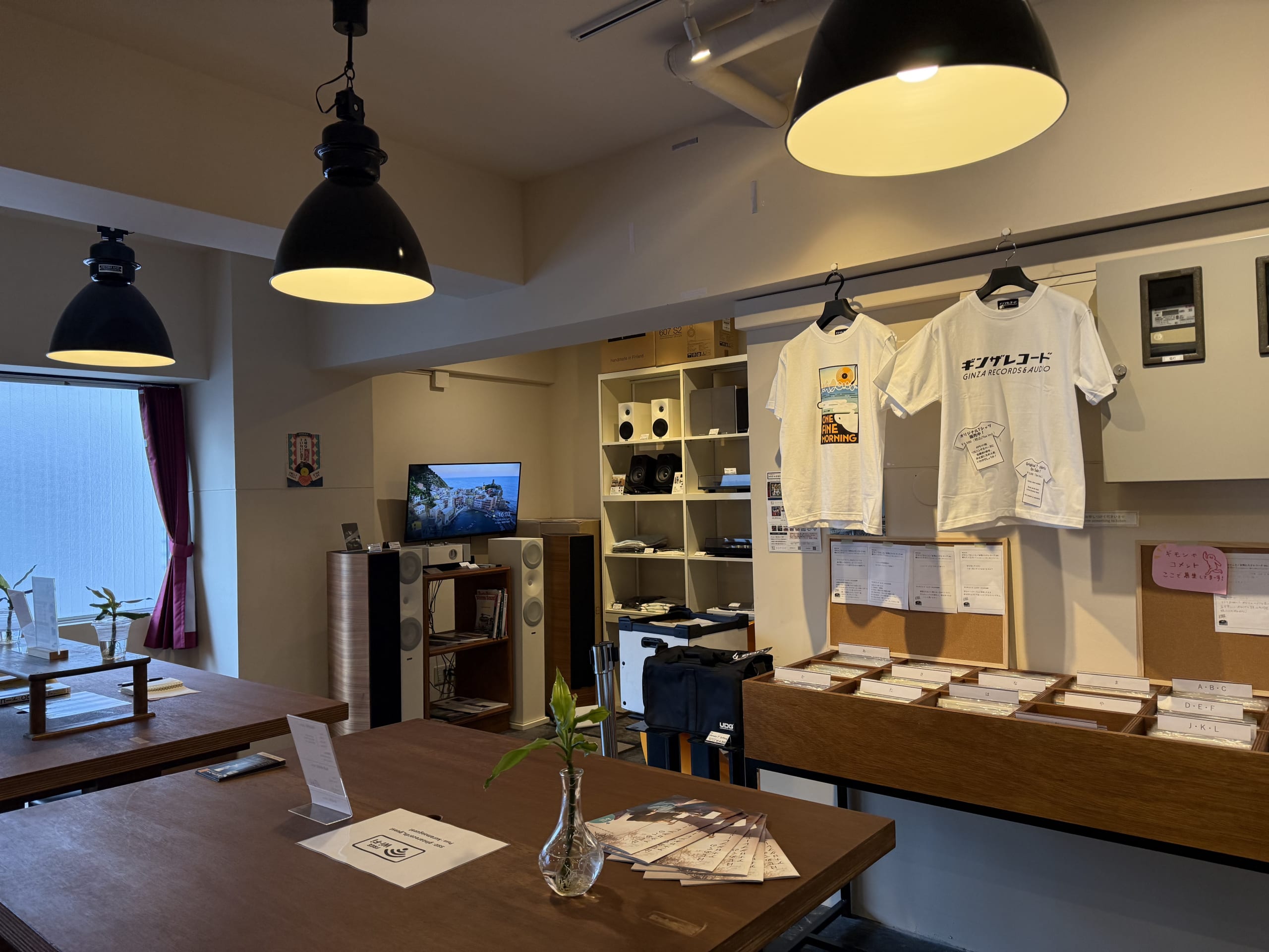 温かな照明が照らすレコード店の店内。木製テーブル、スピーカー、アルファベット順のレコード棚。