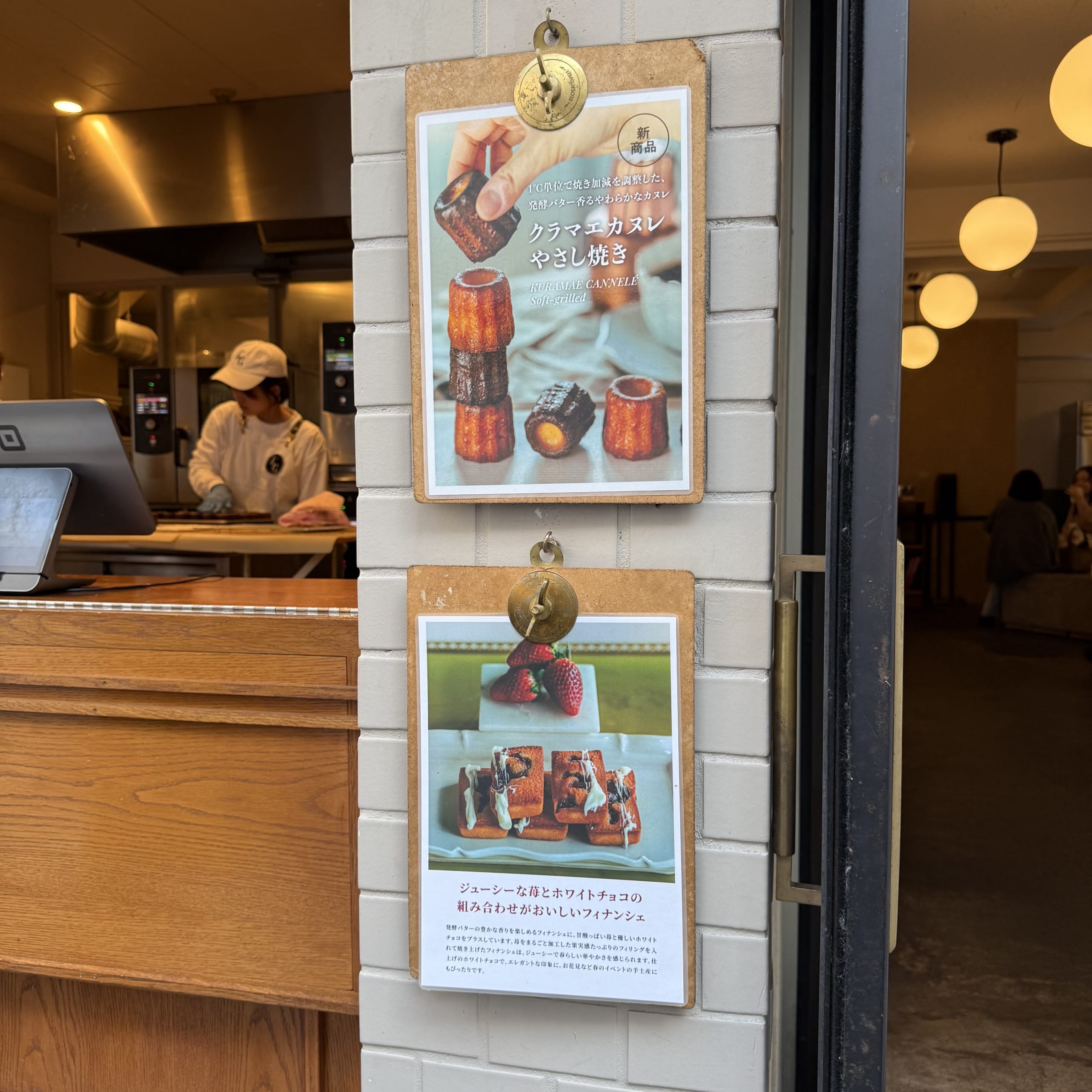 クラマエカヌレの入口。白いレンガ壁のメニューと奥のキッチン、イートイン。