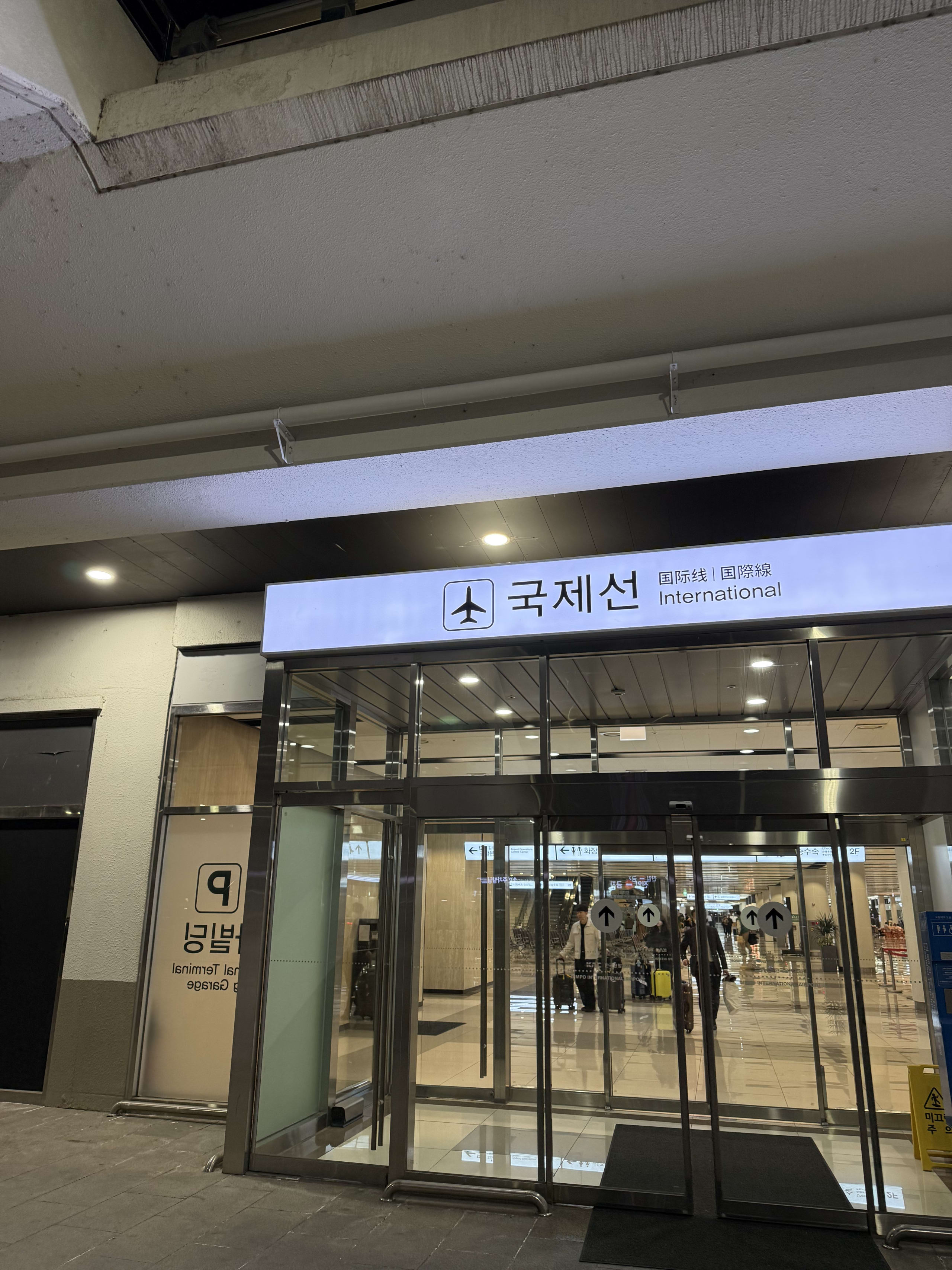 夜の金浦空港国際線のガラス張り出口。駐車場の案内サインが見える。