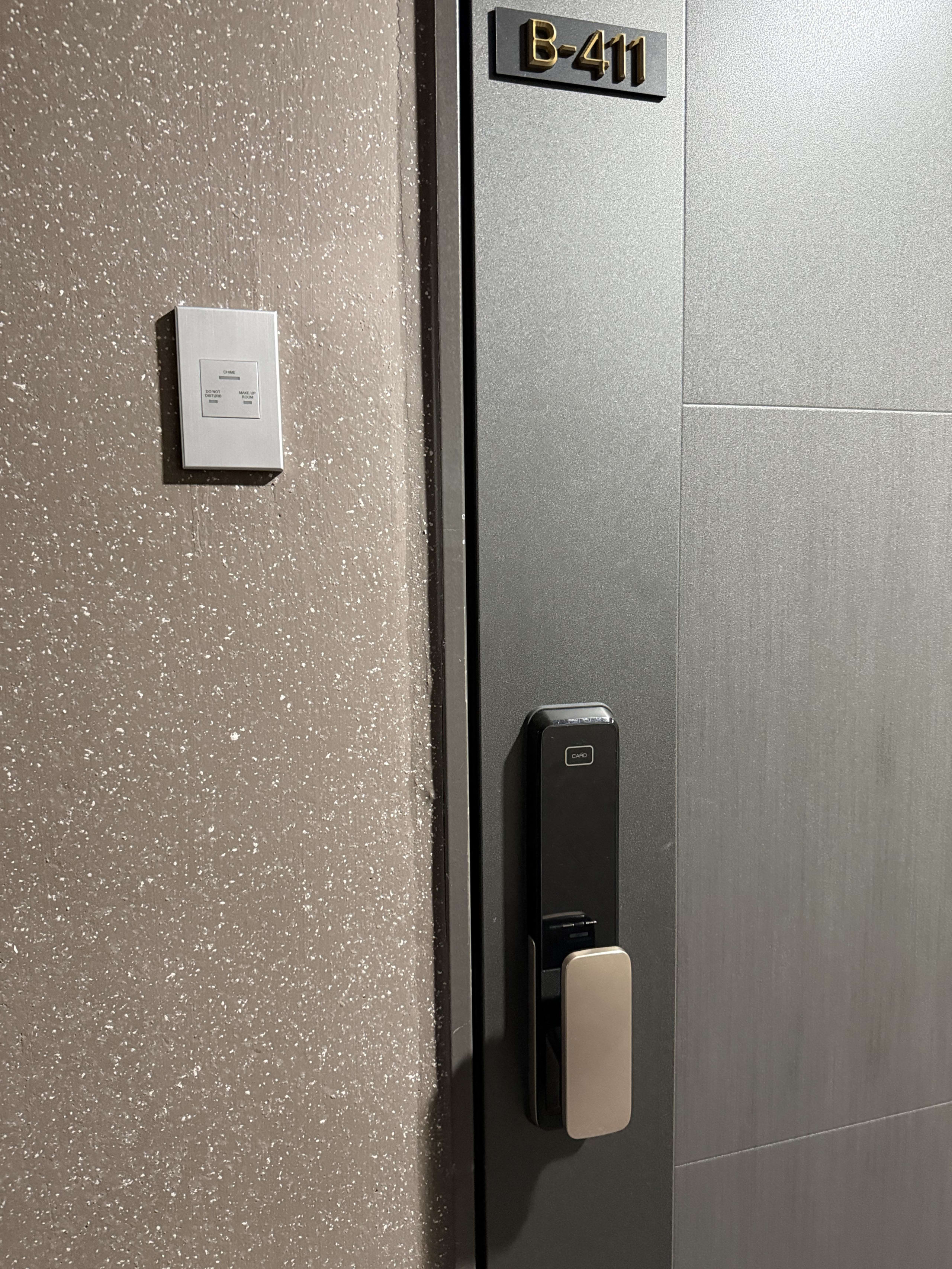 B-411のルームプレートがあるグレーのドアと壁の電子パネル。
