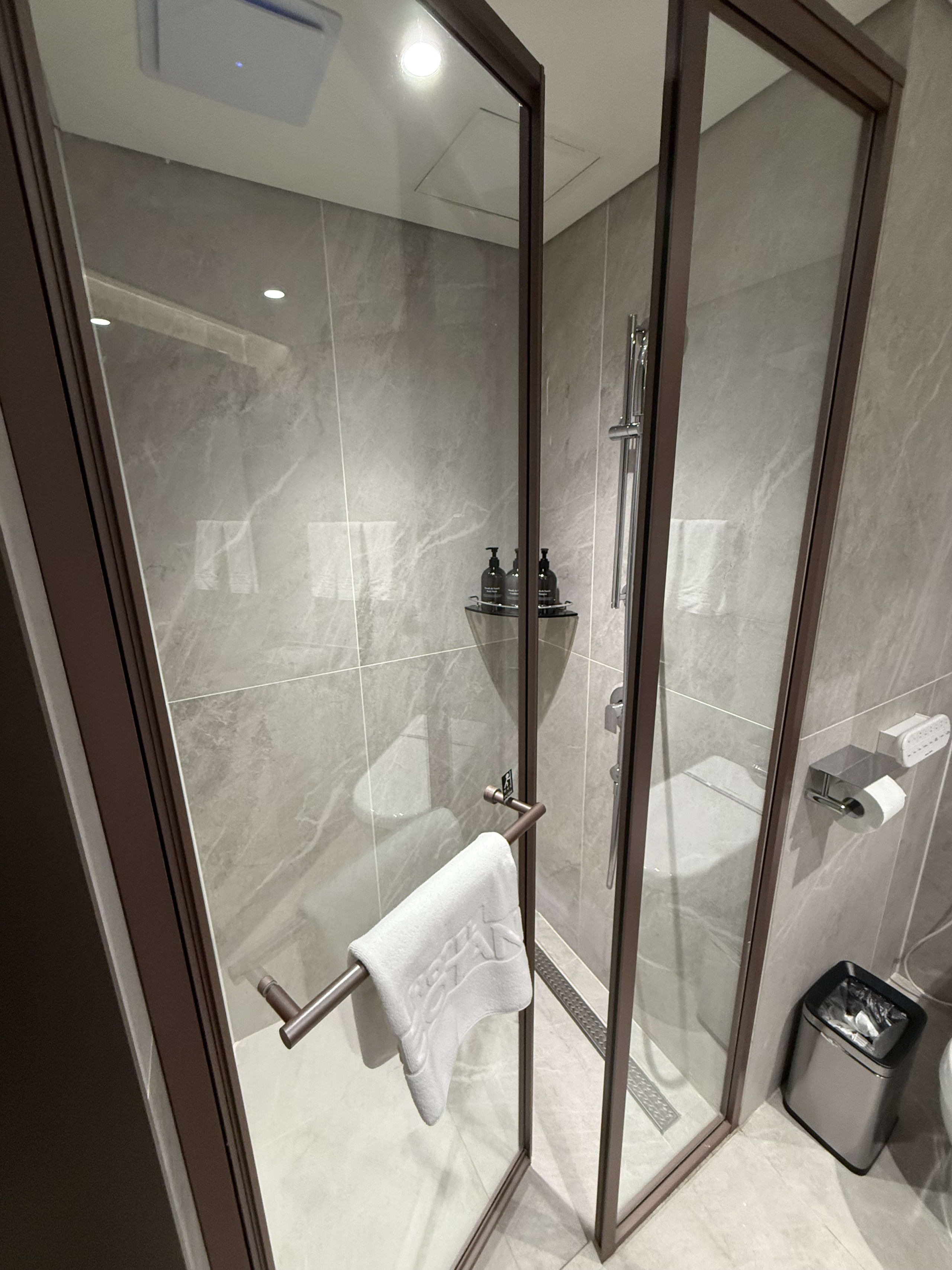 大理石調タイルとガラス扉の清潔なシャワーブース。