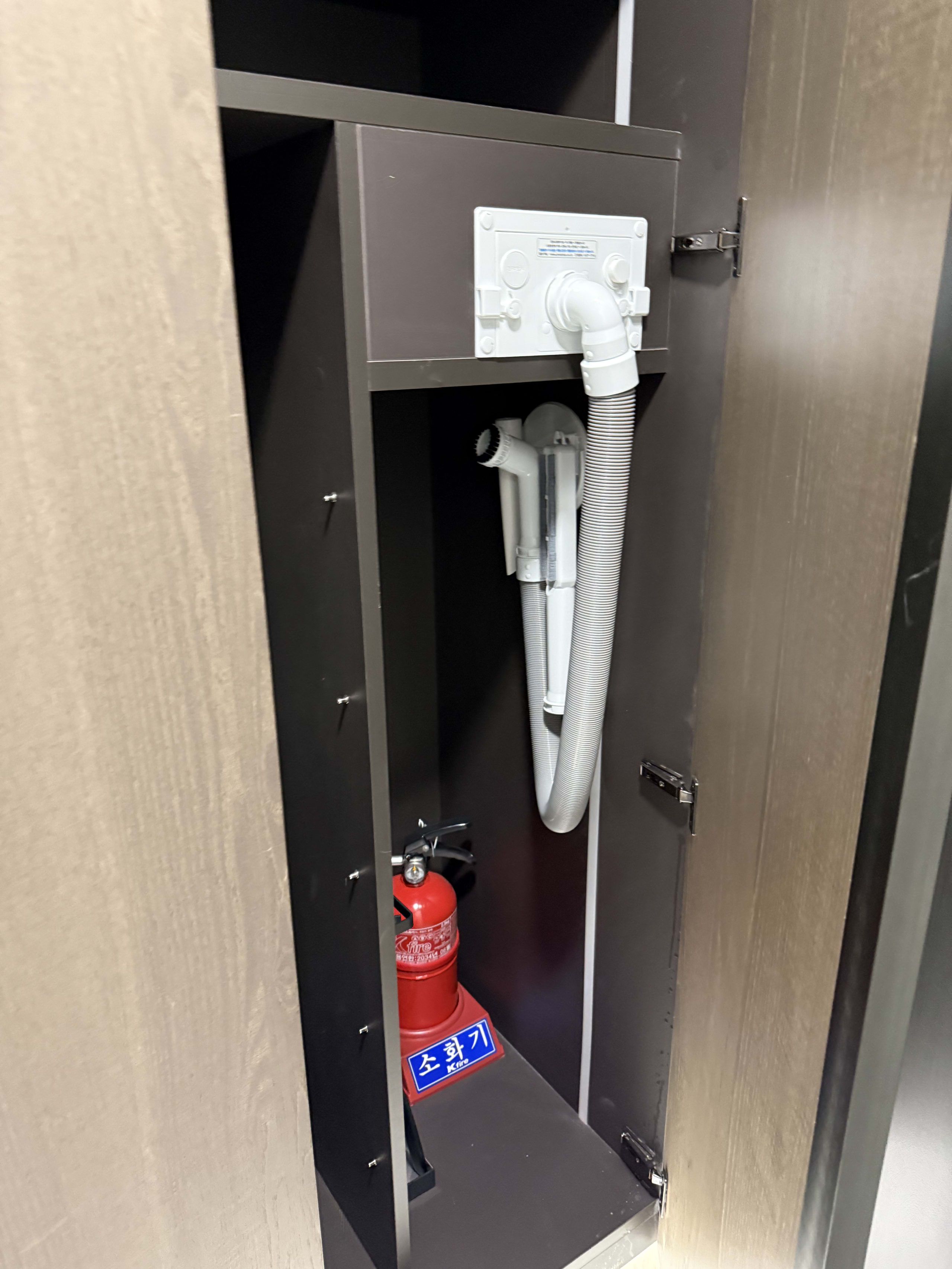棚内のハングル表記の消火器と壁備え付けの白いホース。