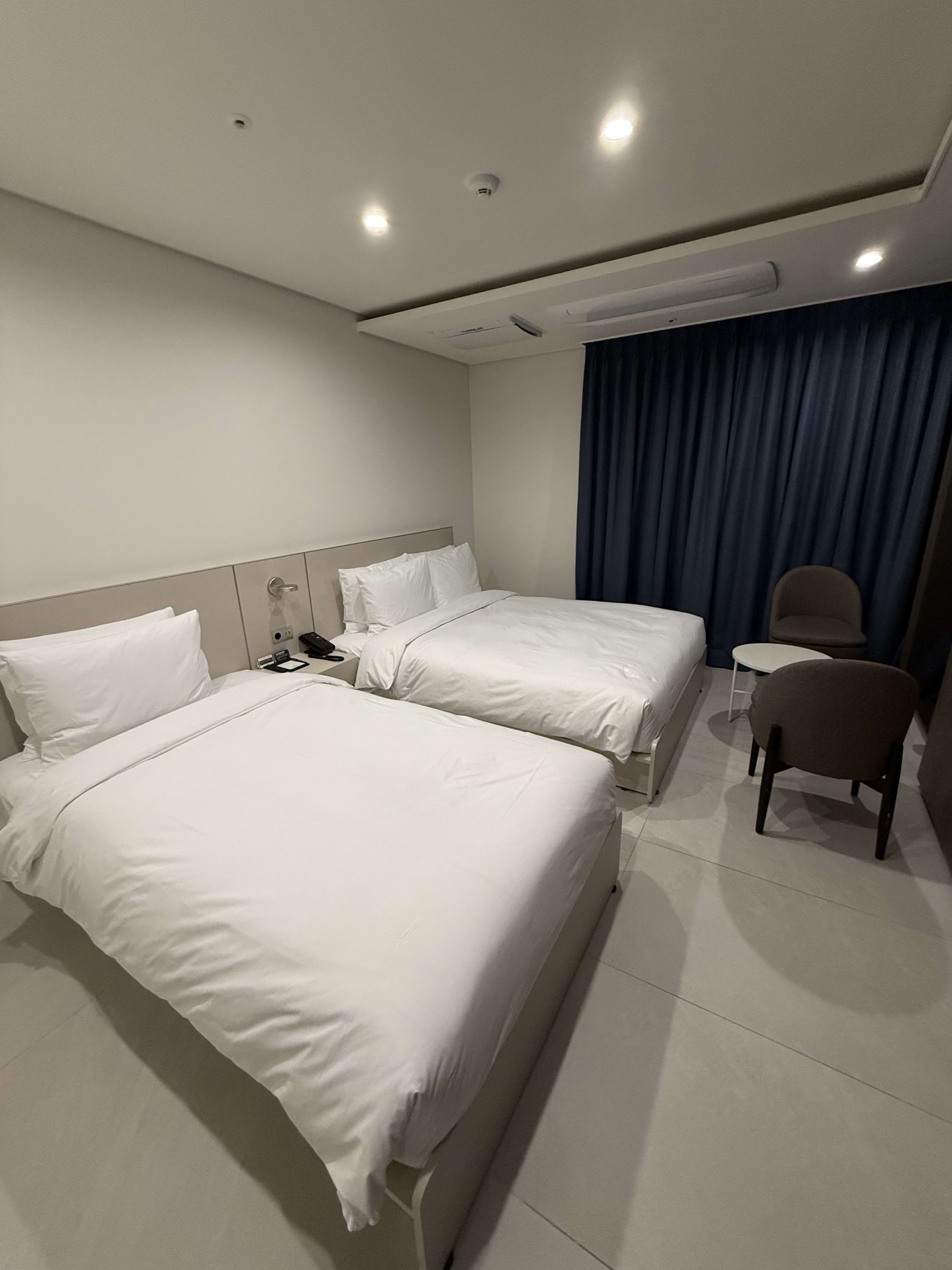 白いベッド2台と青いカーテンがあるシンプルな部屋。