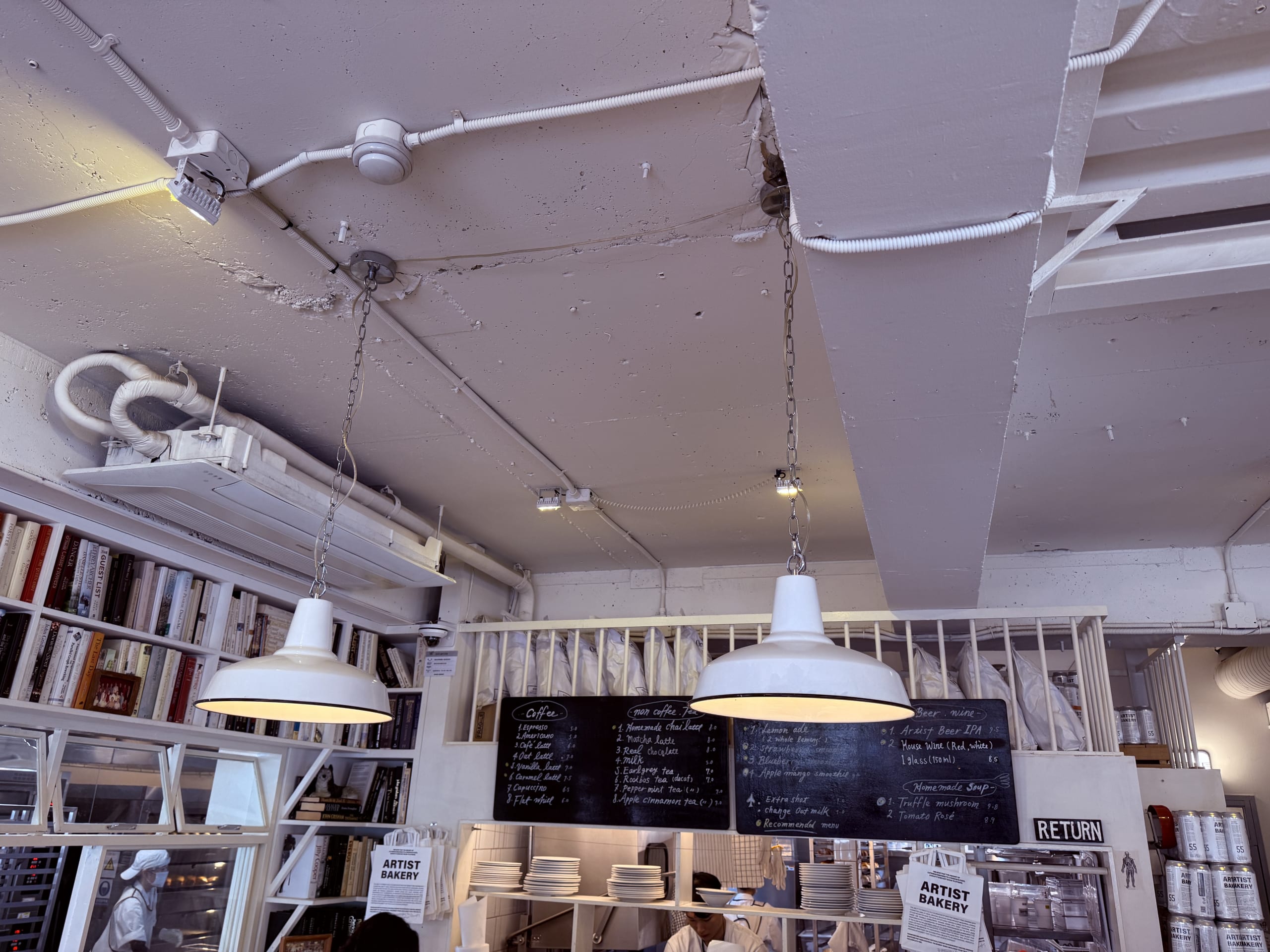 白い天井のライト、黒板メニュー、本棚があるベーカリー店内。