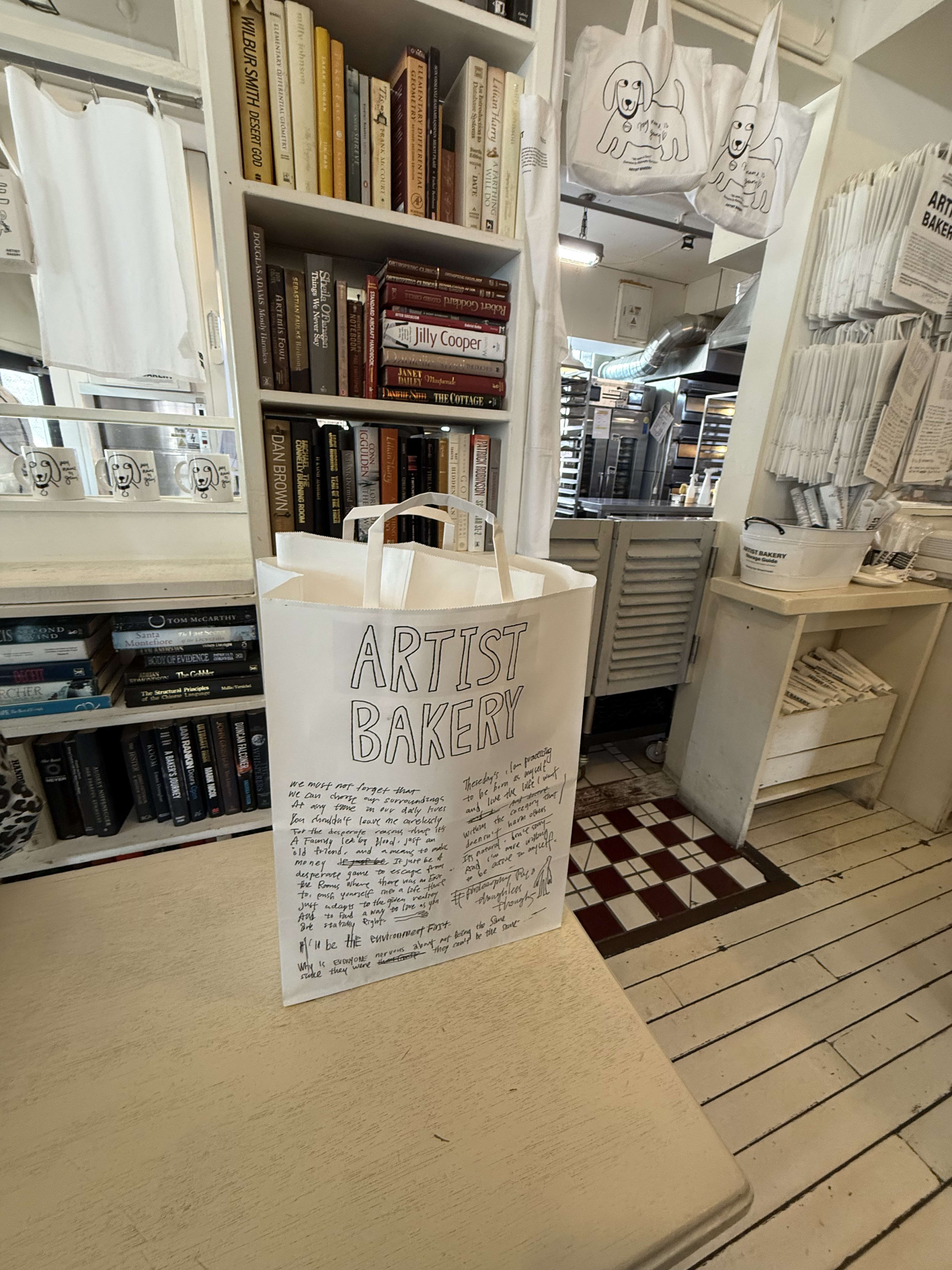 テーブルの上のARTIST BAKERY紙袋。背景に本棚と厨房。