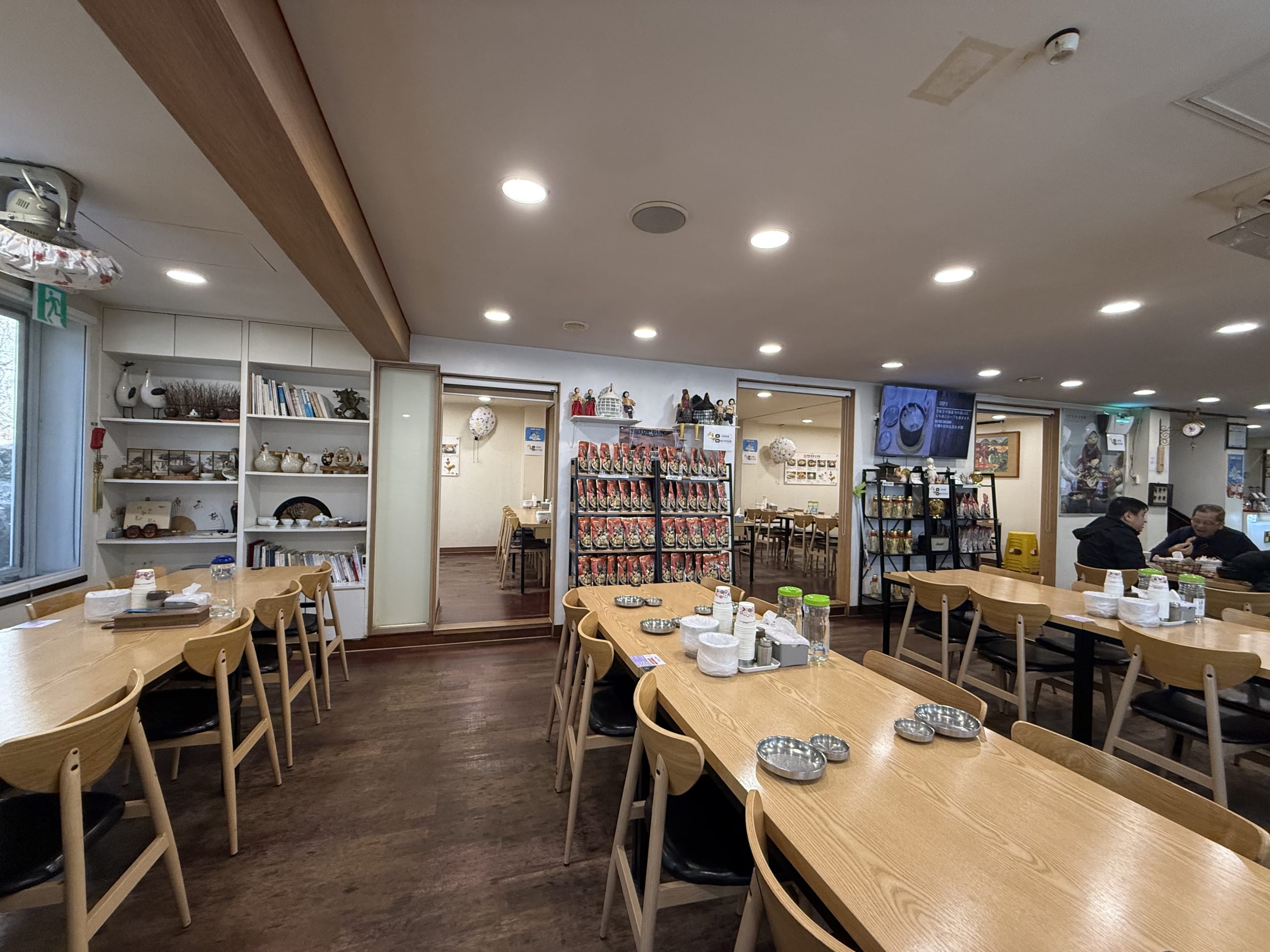 木製のテーブルが並ぶ食堂。棚には鶏の置物や赤い商品がある。