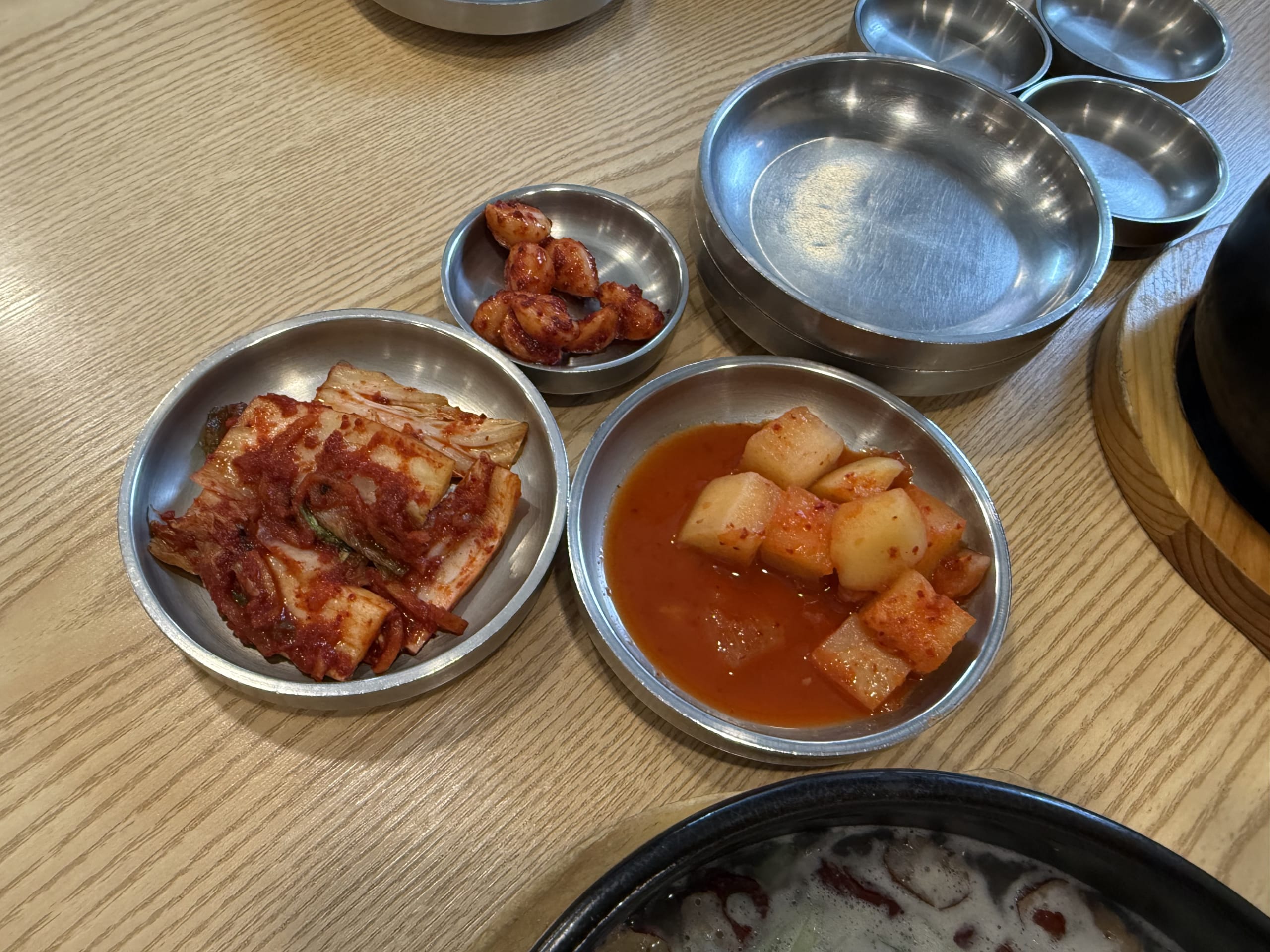 木目テーブル上の3種のキムチと煮え立つ参鶏湯の土鍋。