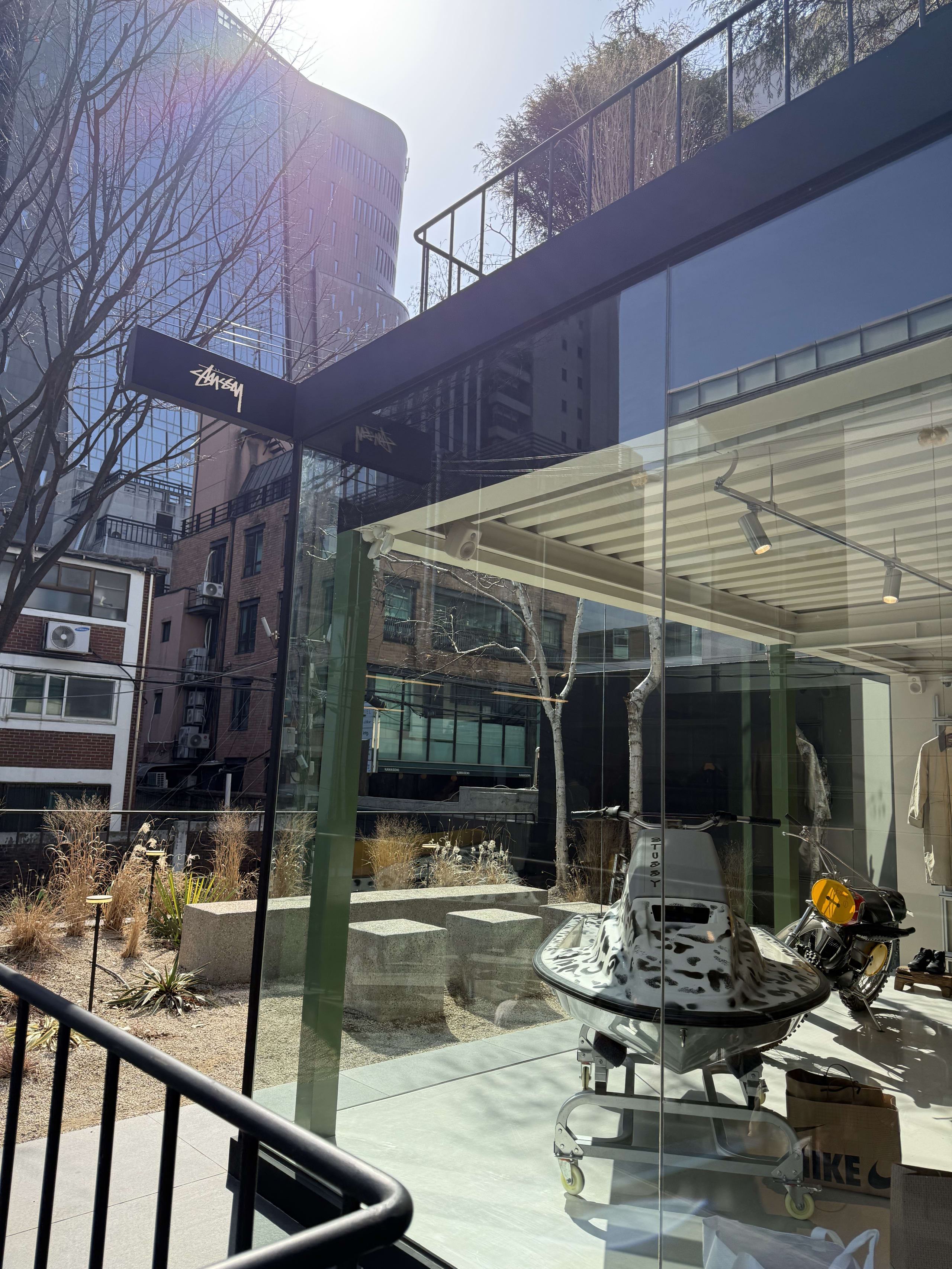 太陽光が反射するStussy Seoul外観。ガラス越しに水上バイクが見える。