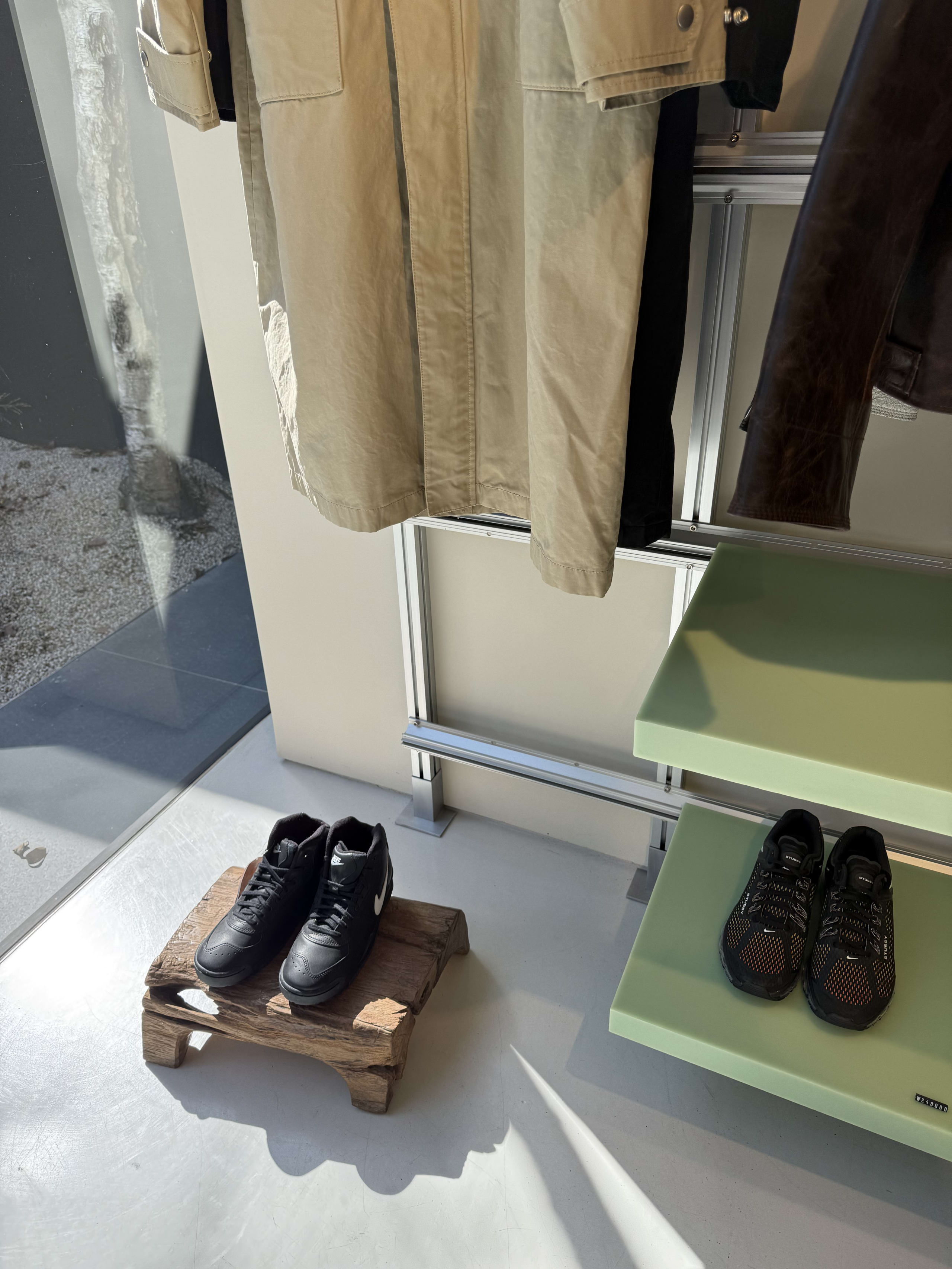緑の棚と木製台座に展示された黒のStüssy×Nikeスニーカー。