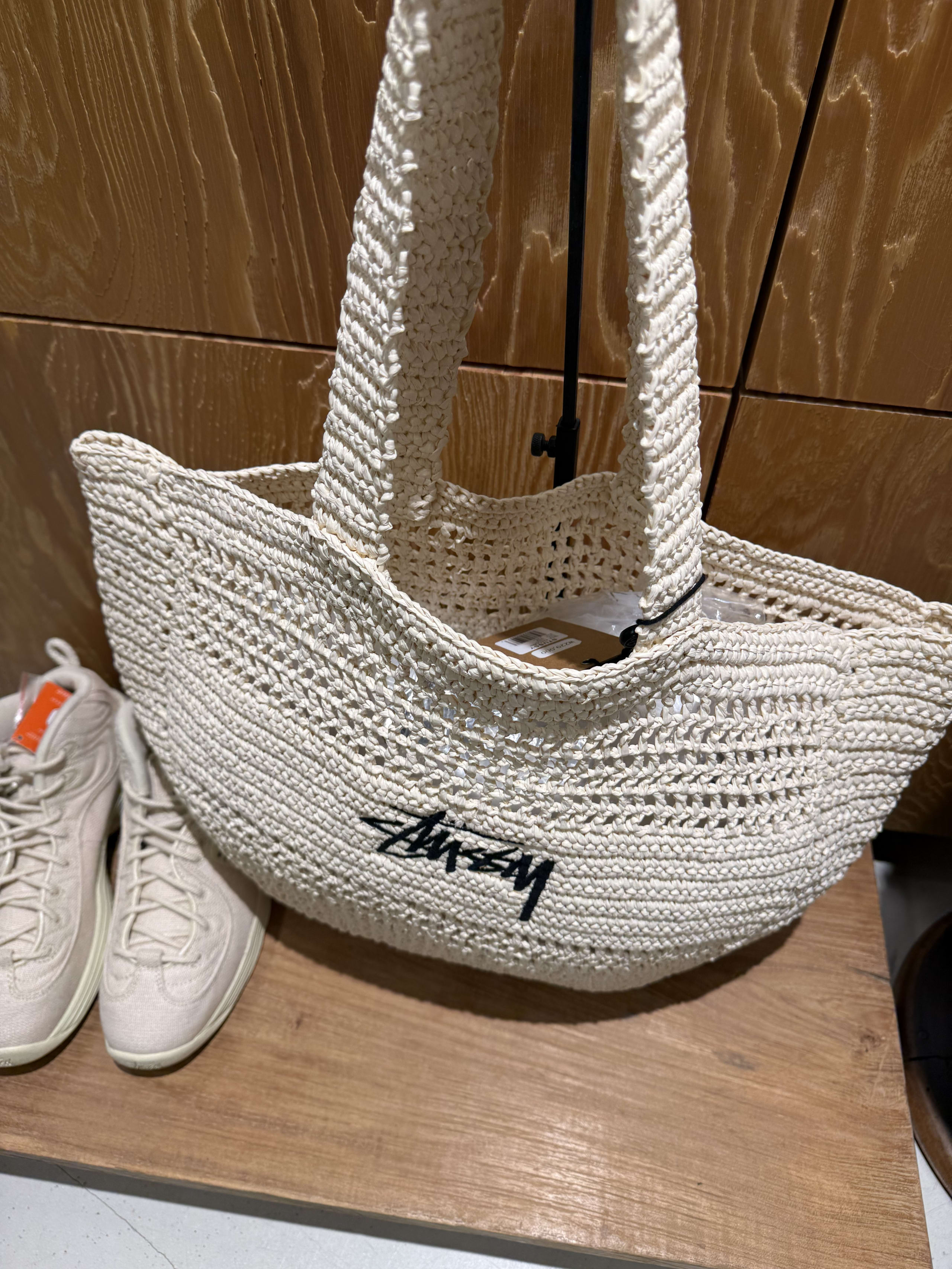 Stussyのラフィア風トートバッグとNikeスニーカーの展示。