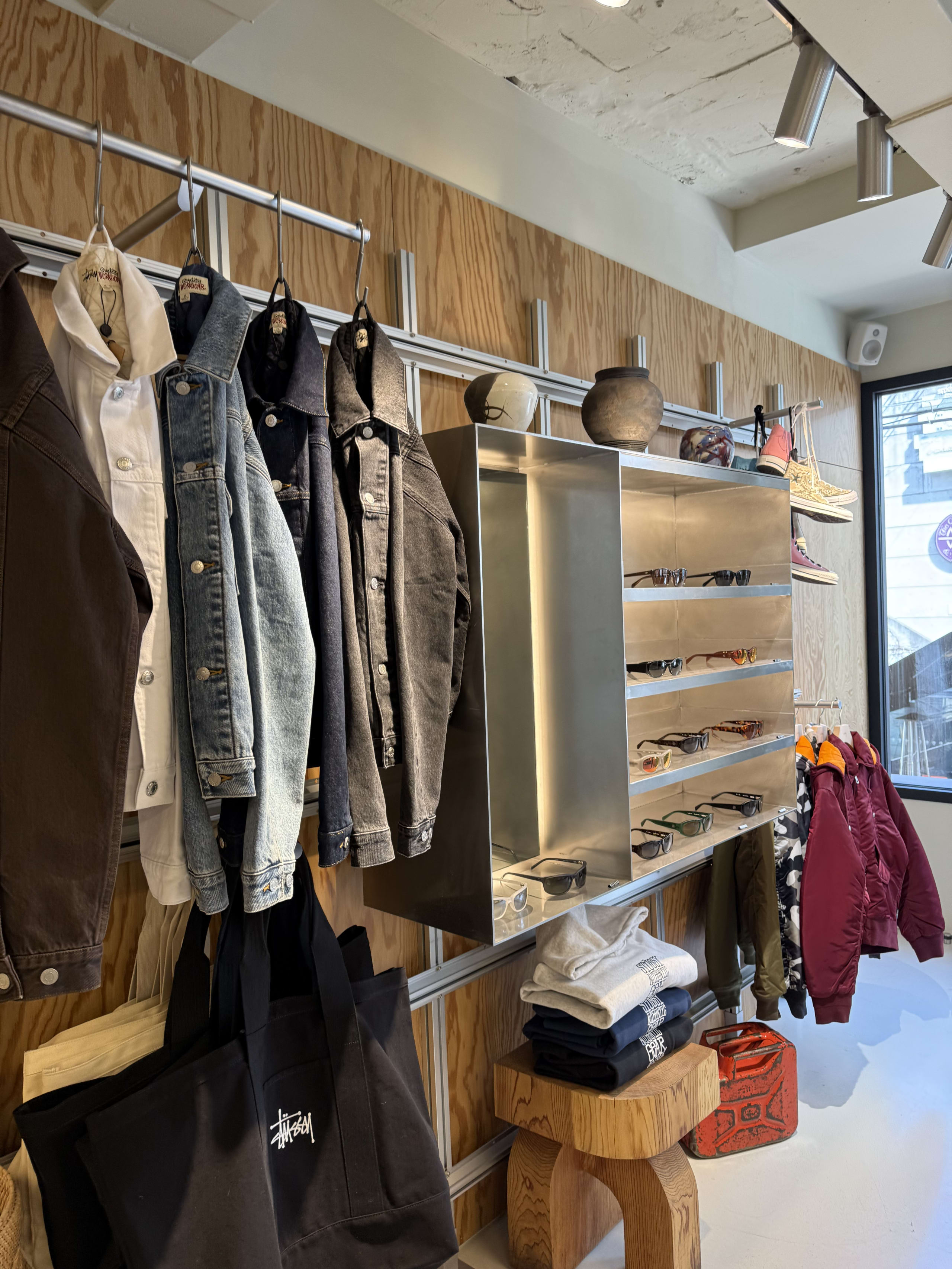 木目壁と金属棚が並ぶStussy Seoul店内。ジャケットや小物の陳列風景。