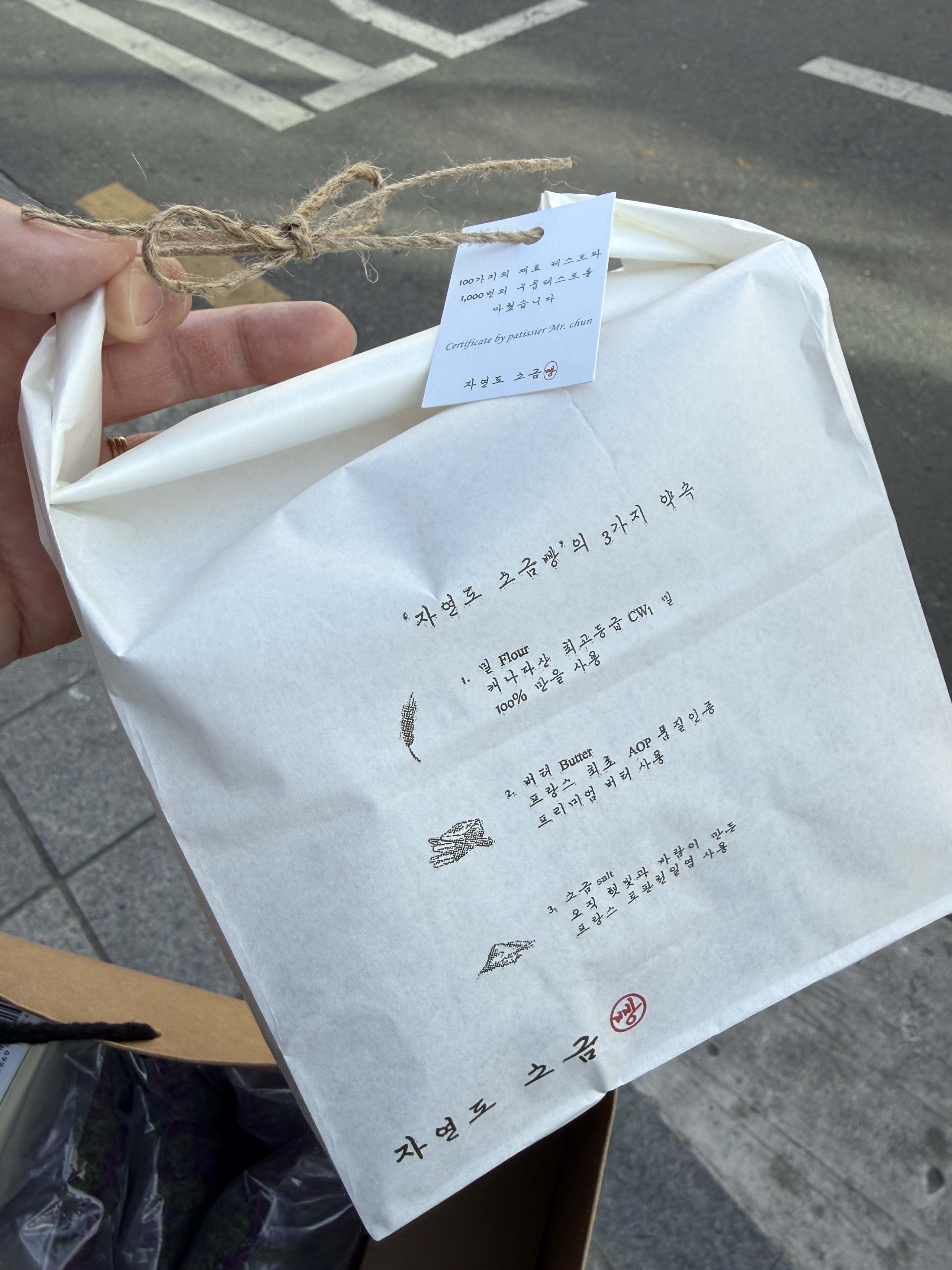 路上で麻紐で結ばれた自然島塩パンの白い紙袋を持つ手。