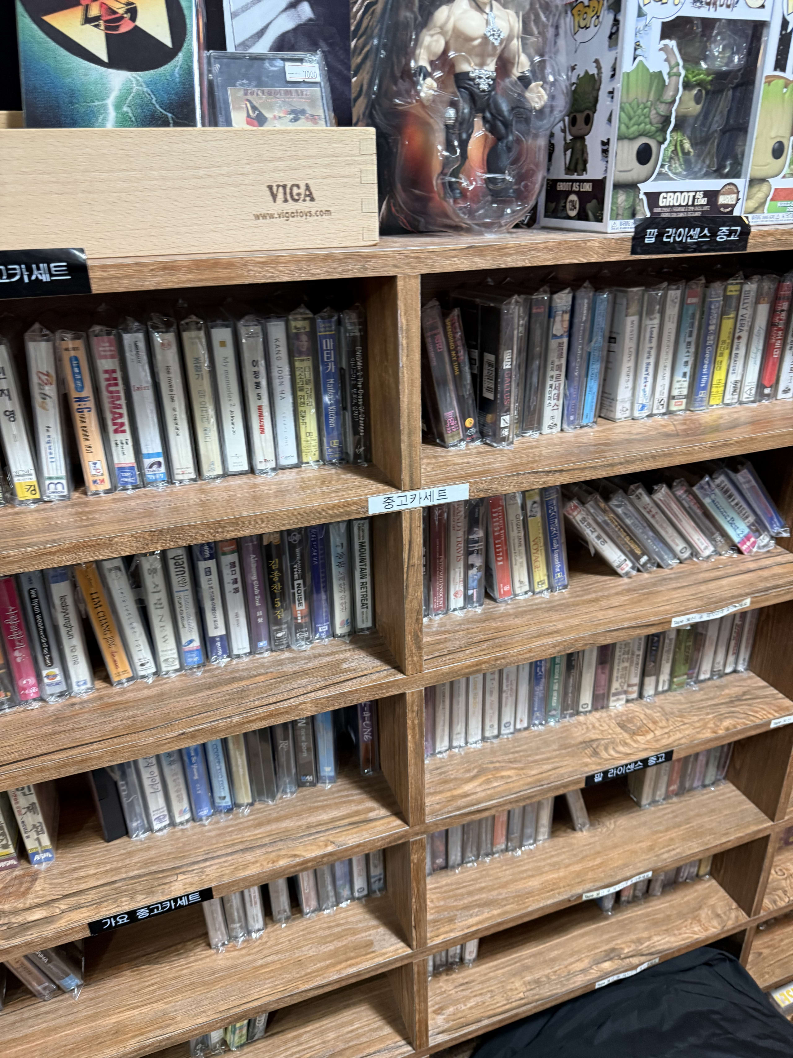 木製棚に並ぶ大量の中古カセットテープとフィギュア