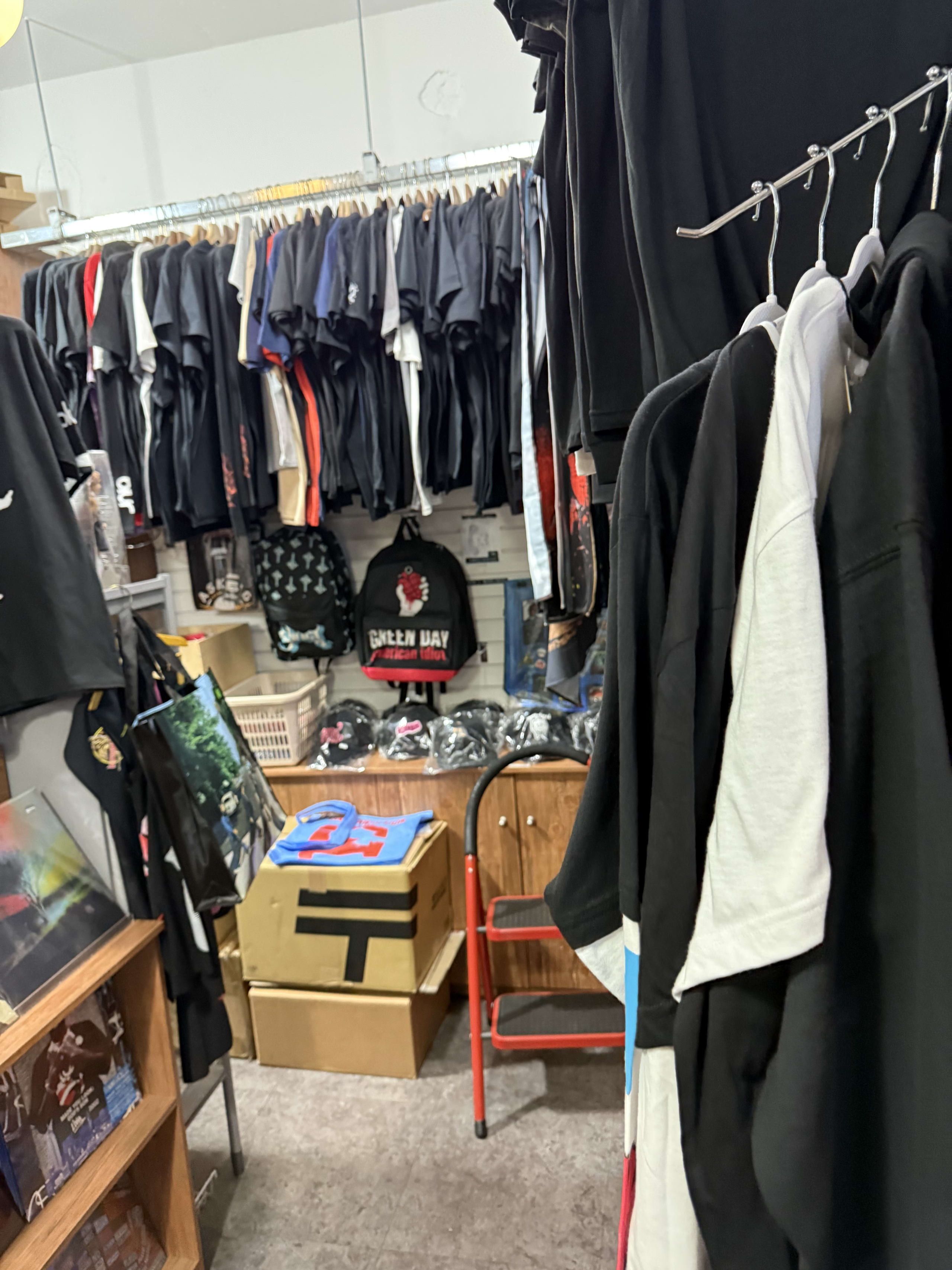 壁一面のバンドTシャツ、リュック、段ボール、赤い脚立。