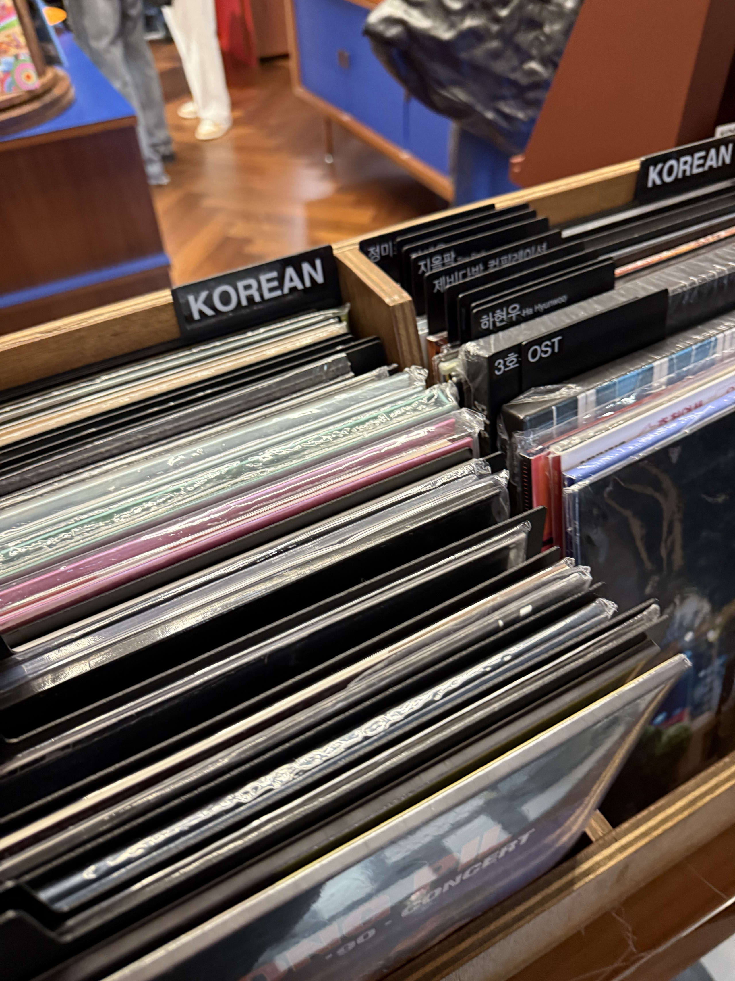 「KOREAN」の仕切り板がある木製レコードラックと新品レコード。