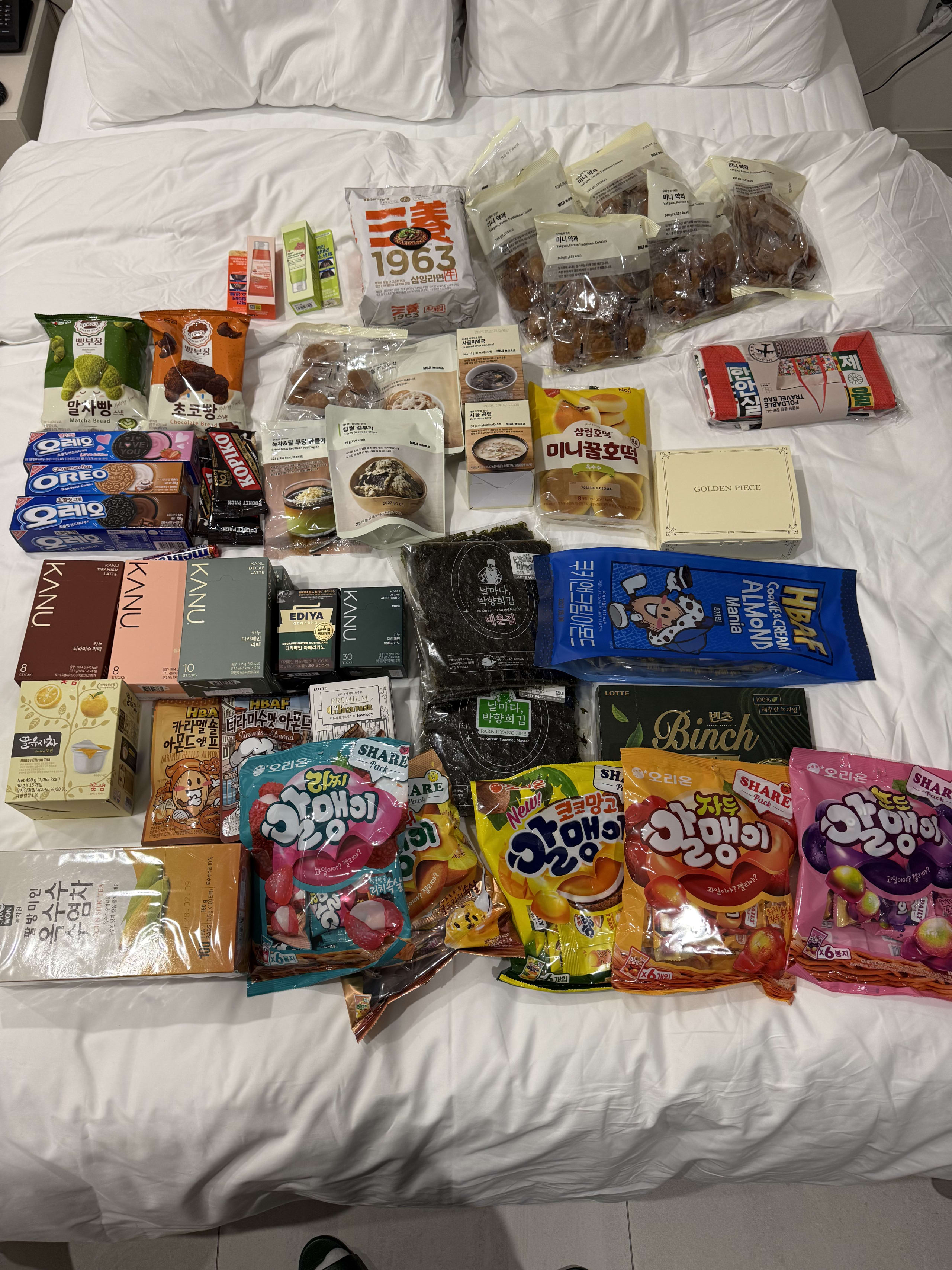 白いベッドの上に並ぶ韓国土産の菓子やコーヒー、お茶、海苔。