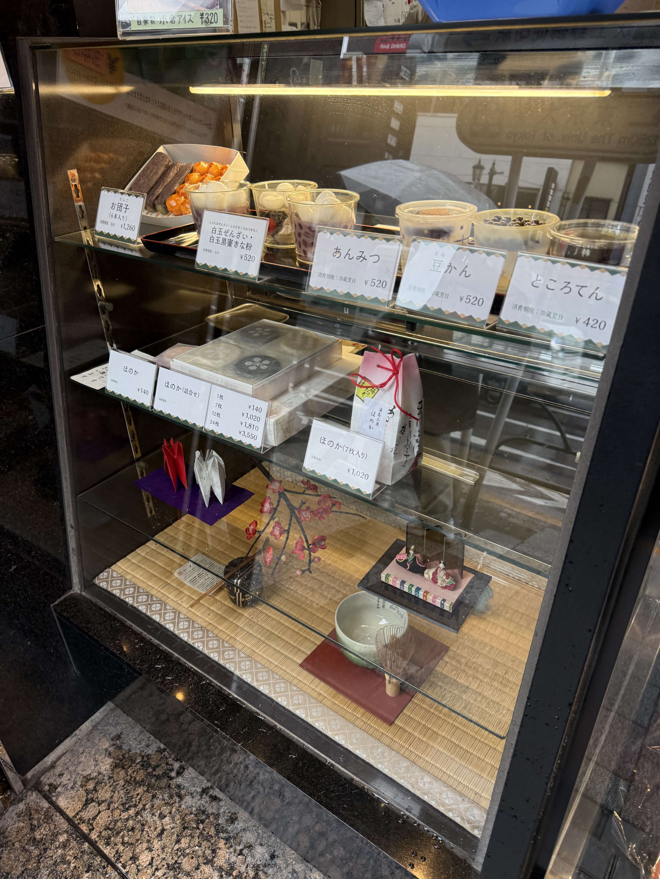 和菓子店のショーケース。あんみつや豆かん、季節の飾りが並ぶ。