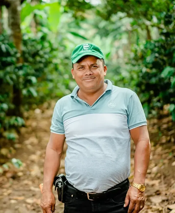A man smiling and wearing a Raíz Sustainability® hat walking on a trail in the woods