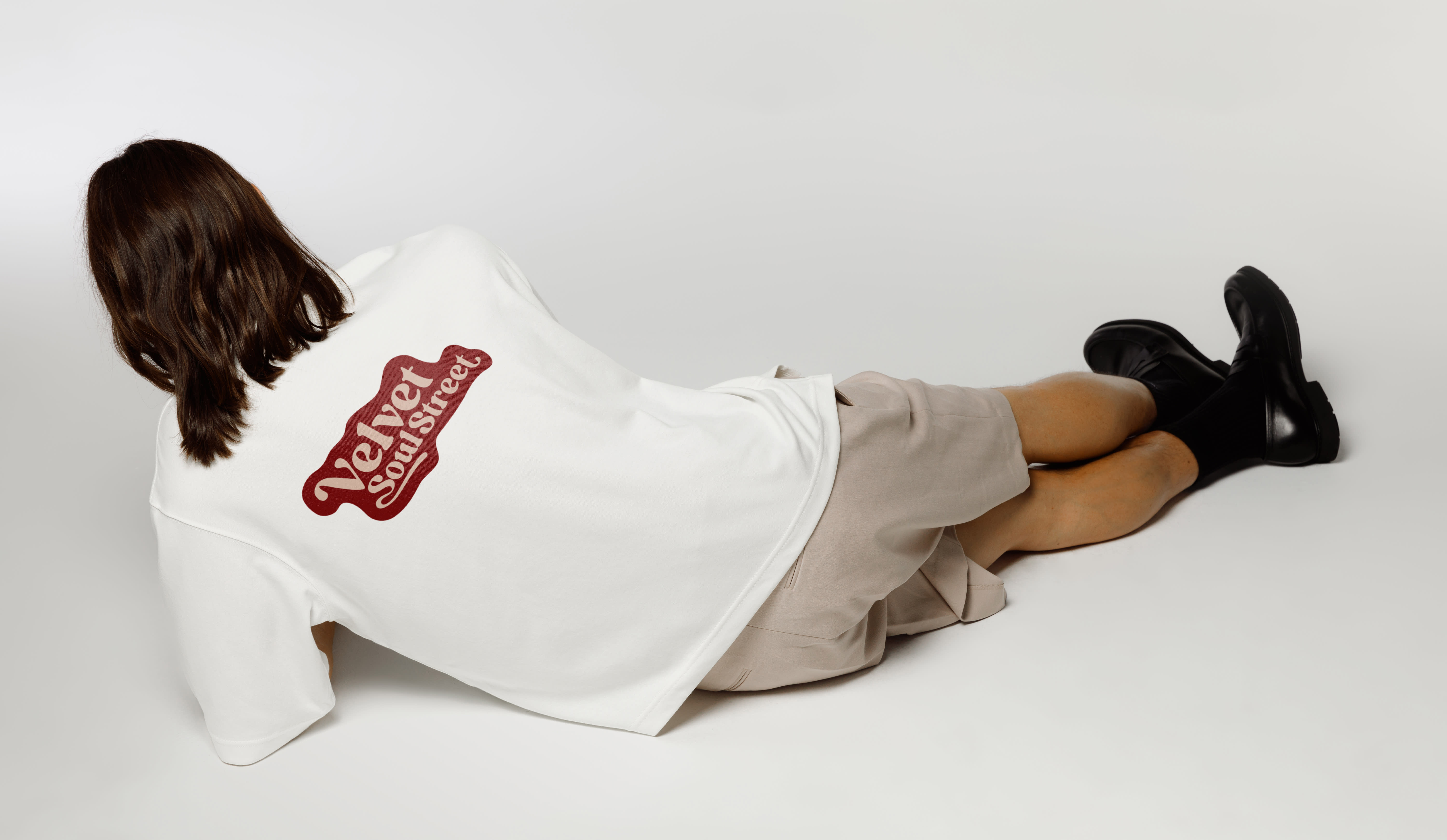 A man is lying on the ground, wearing a shirt with a logo. The logo shows the corporate design of the band Velvet Soul Street.