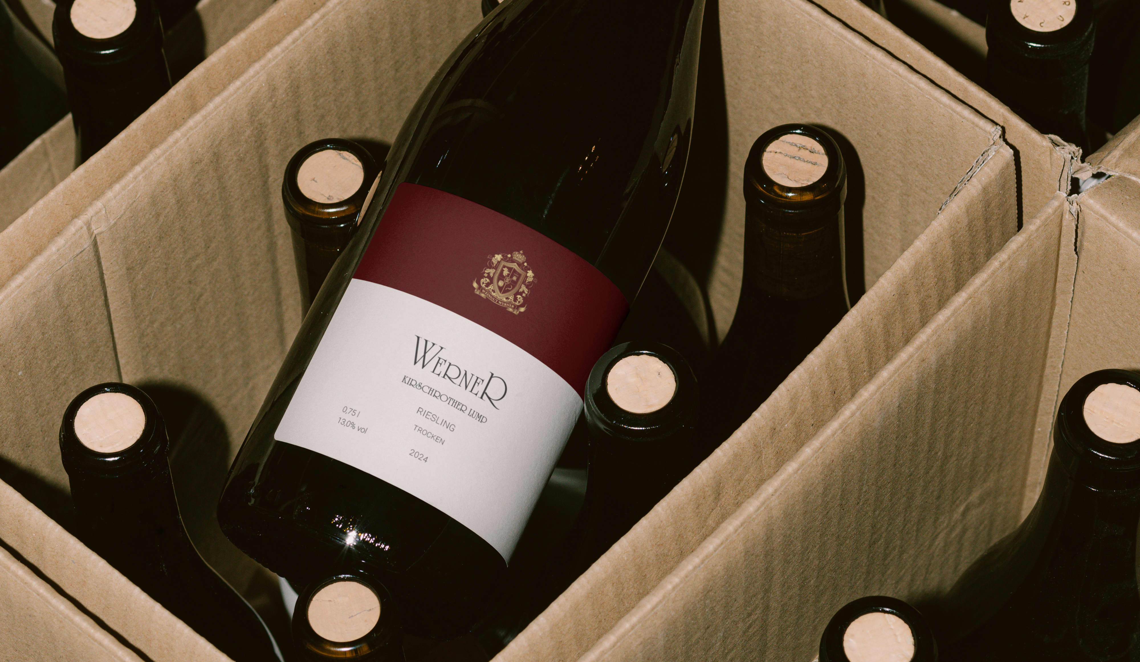 An open box of wine bottles can be seen from above. One of the bottles has already been taken out and the label is visible. It reads Weingut Werner with a dark red and white label.