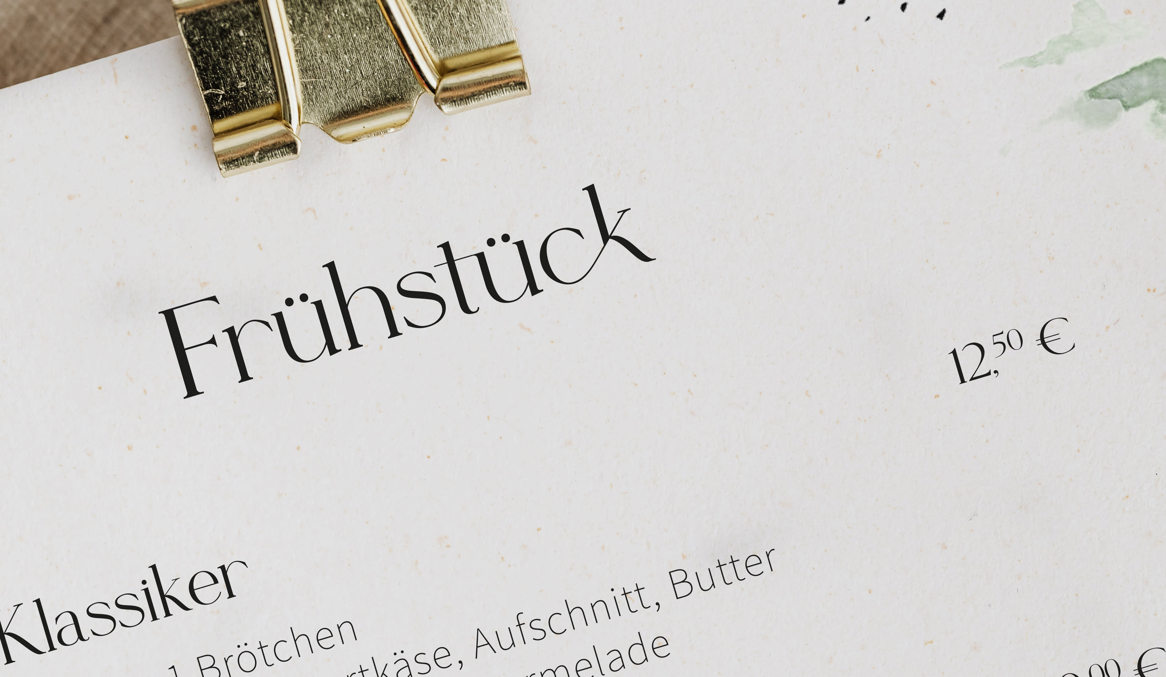 Es ist eine Nahaufnahme der Menükarte von Leni's zu sehen. Mit einer Serifen Schrift und Wasserfarben werden mehrere Gerichte und Details abgebildet.