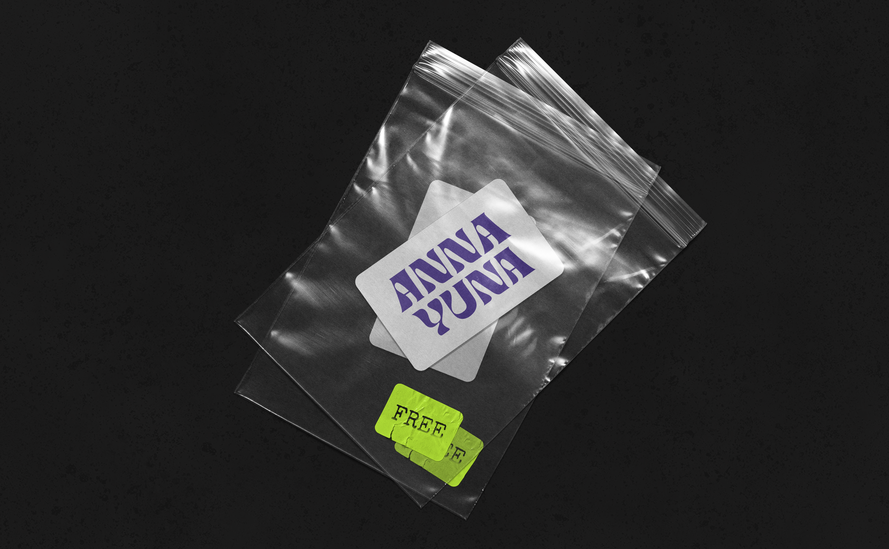 Two small transparent plastic bags are lying on concrete. The bags contain white stickers with the purple lettering ANNA YUNA. They are handed out at concerts.
